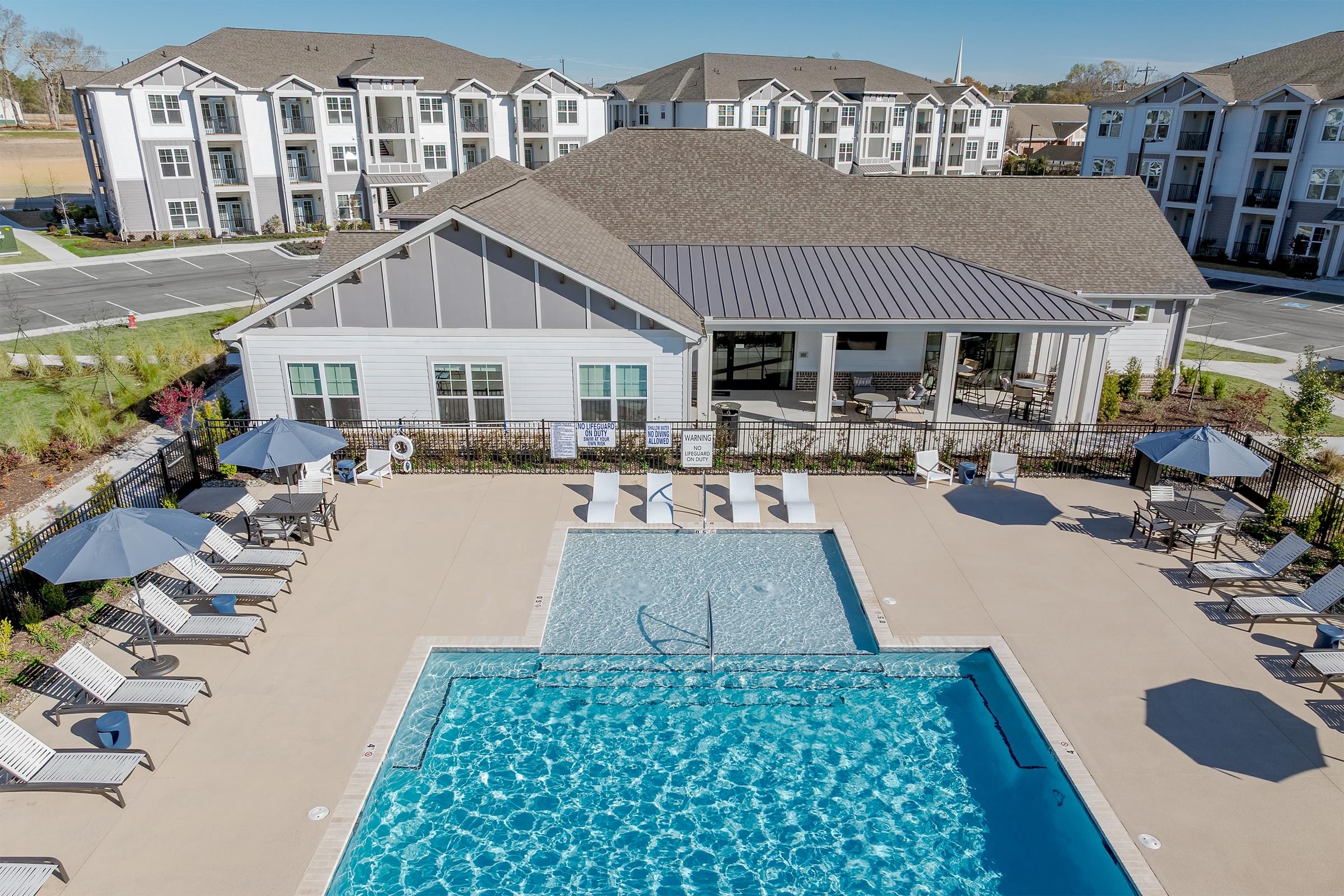 A large swimming pool surrounded by lounge chairs and umbrellas in front of a resort-style building.