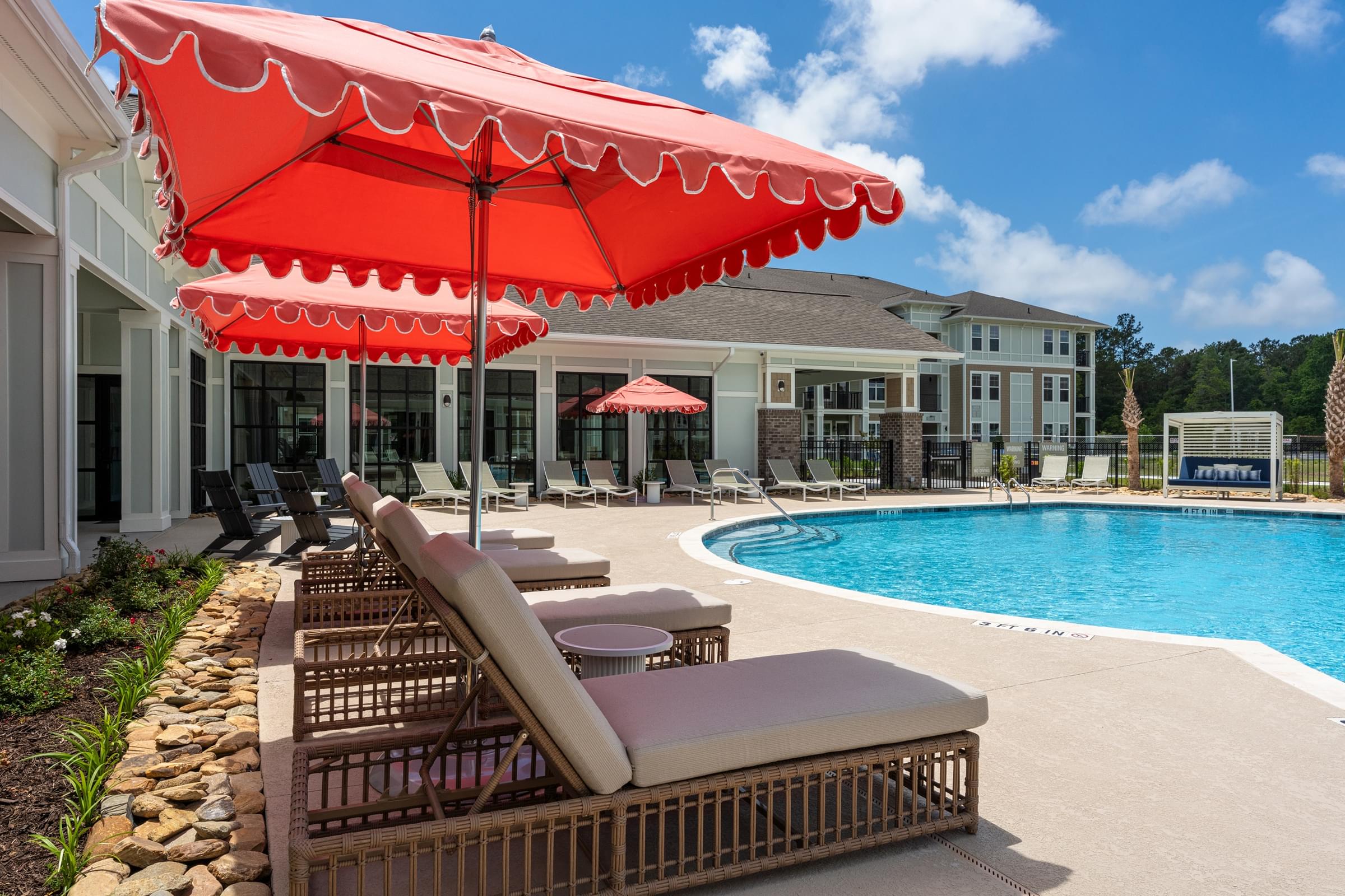 A red umbrella shades a row of lounge chairs by a pool.