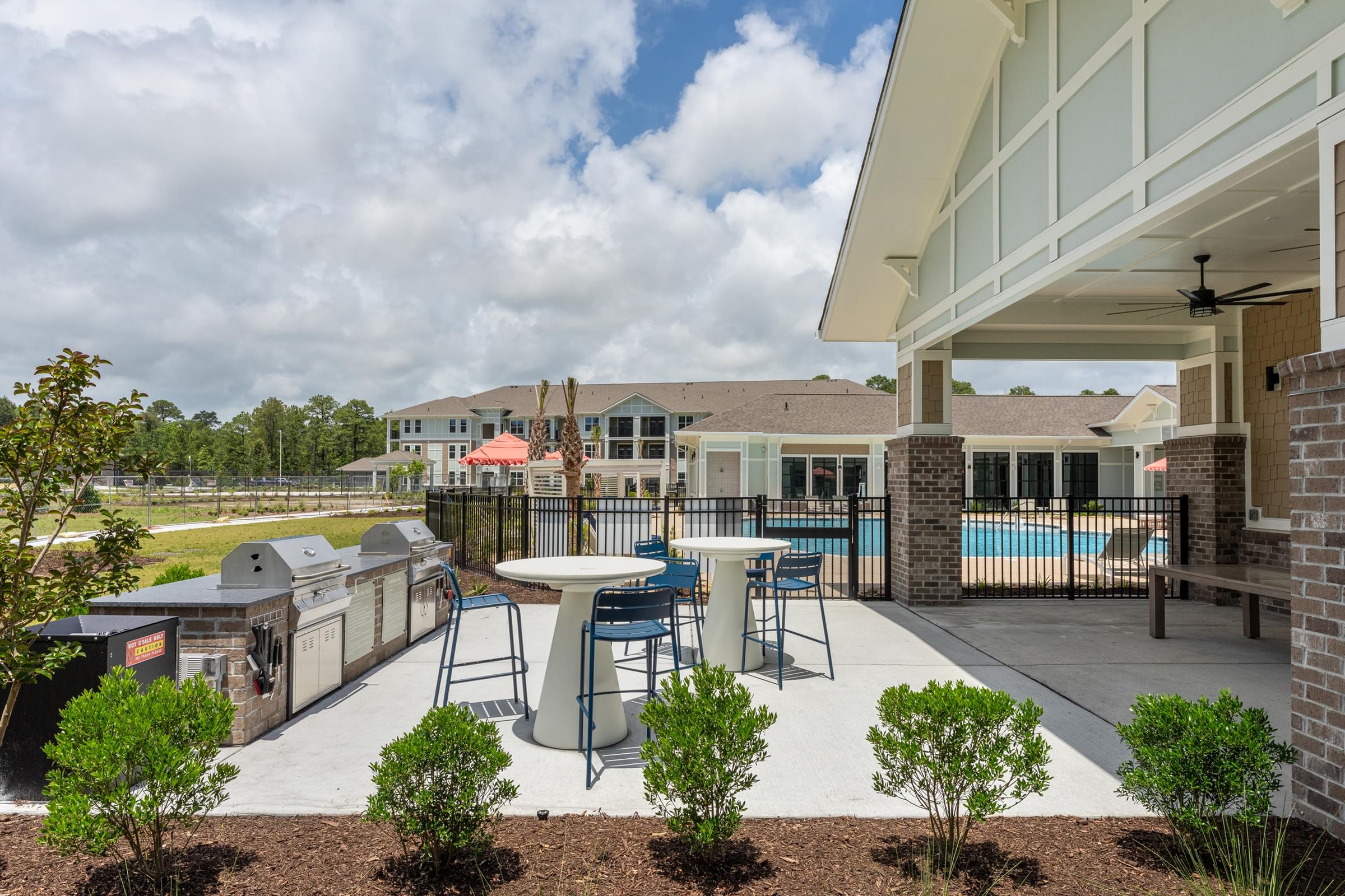 A patio with a table and chairs is surrounded by a pool and a building.