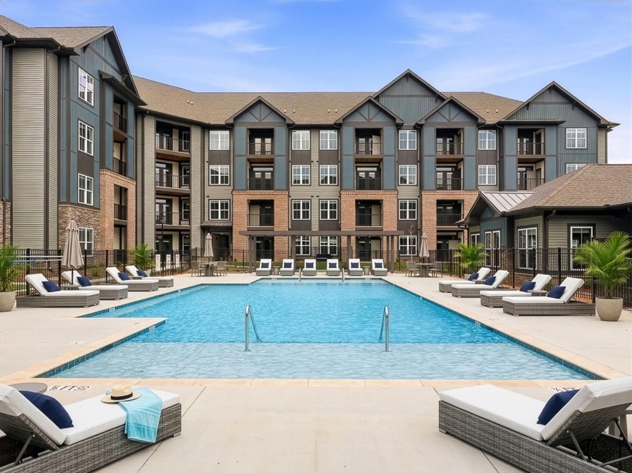 A large swimming pool surrounded by lounge chairs and apartment buildings.