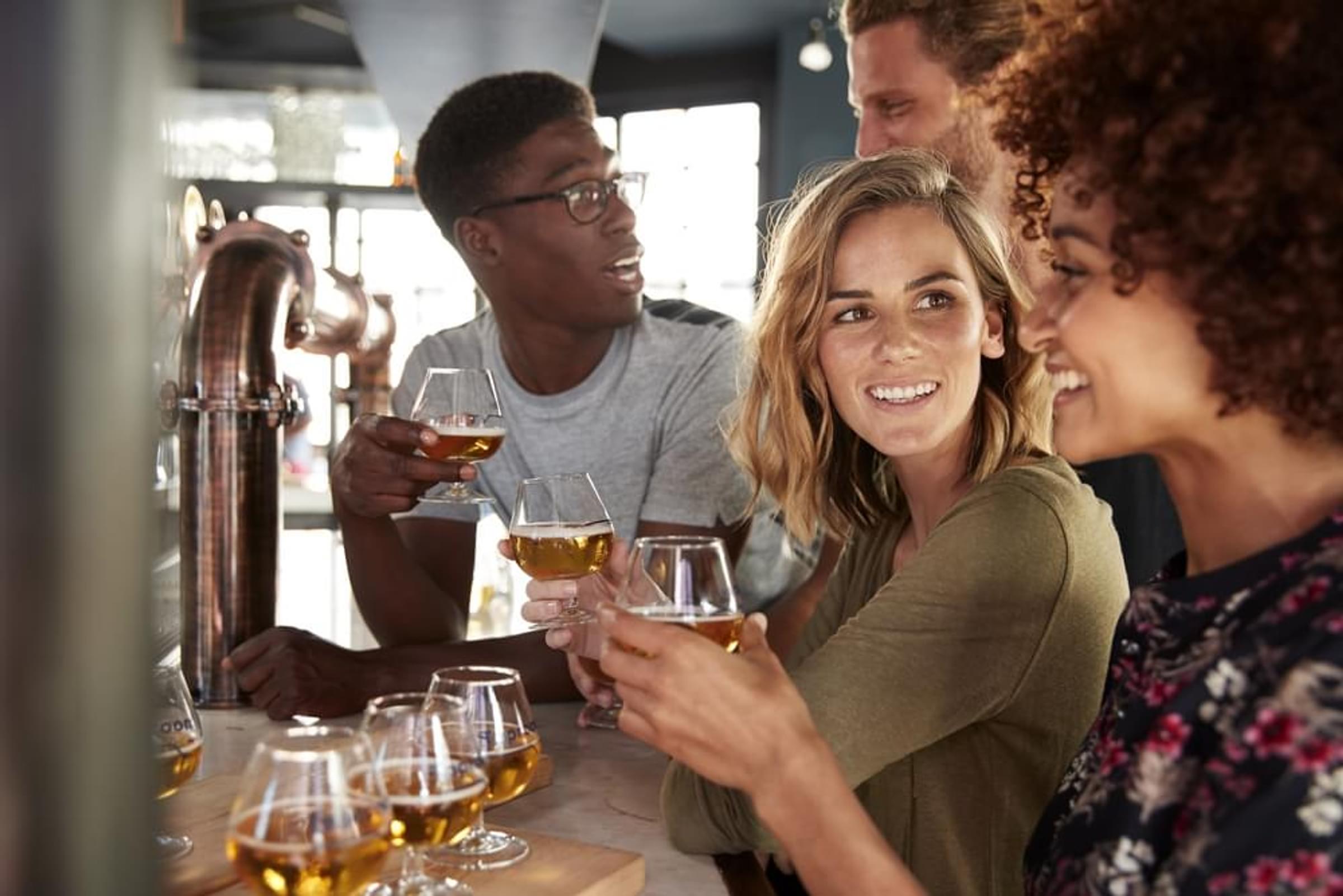 A group of people are gathered around a table, toasting with glasses of beer.