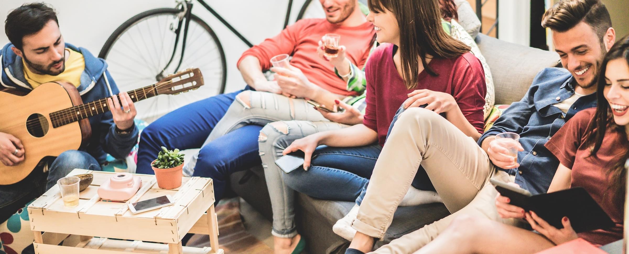A group of people are sitting on a couch, with one person playing guitar and others using their phones.