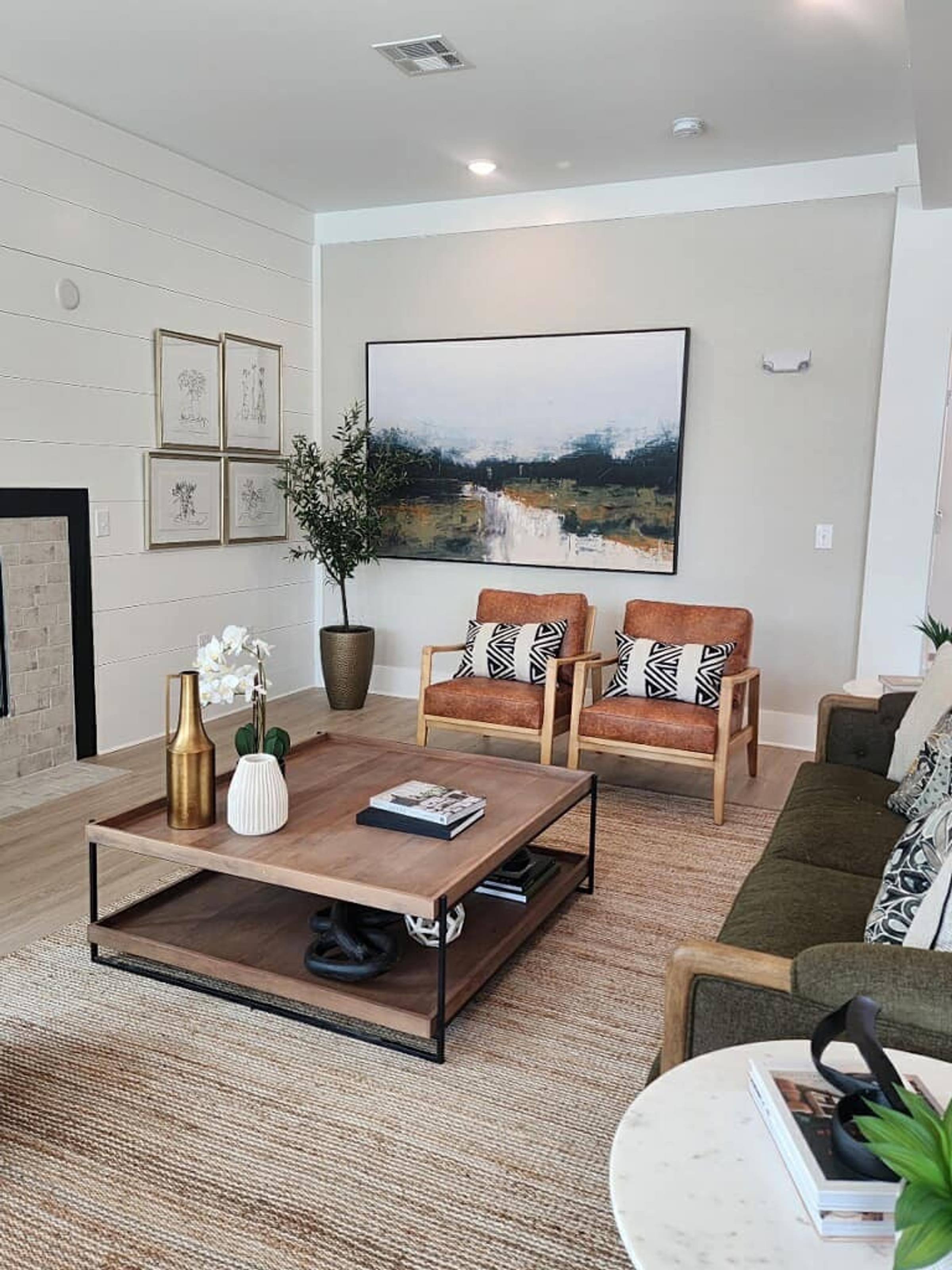A living room with a coffee table, two chairs, and a painting on the wall.