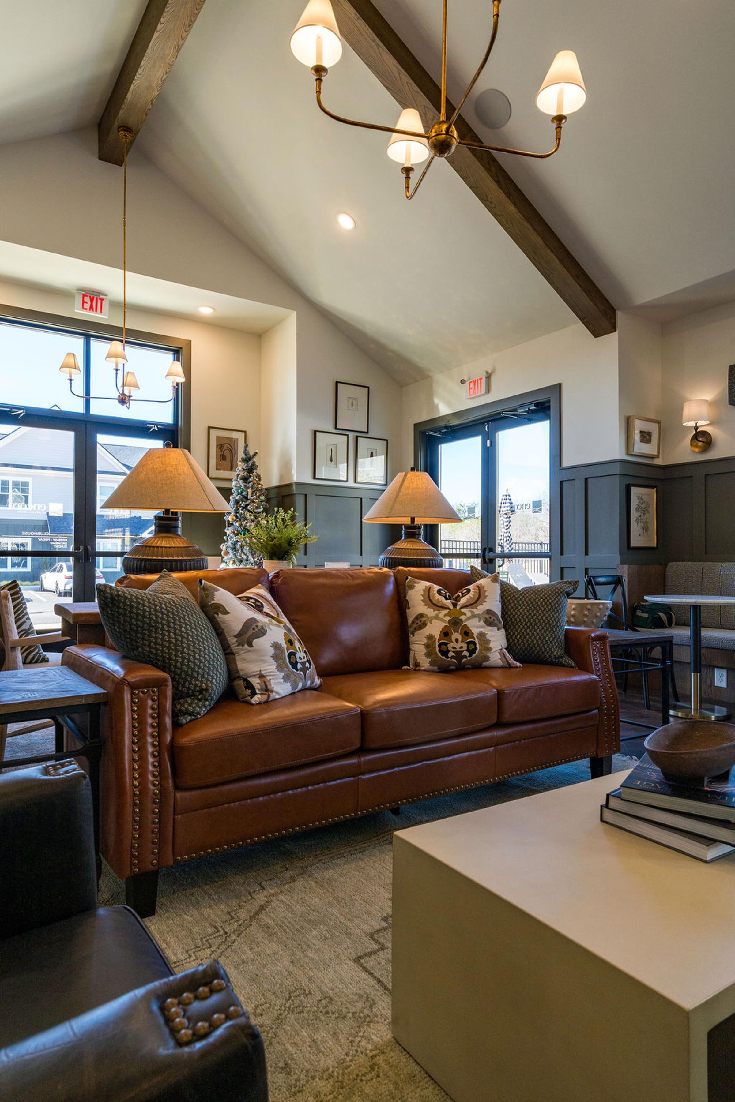 A brown leather couch with pillows sits in a room with a chandelier.