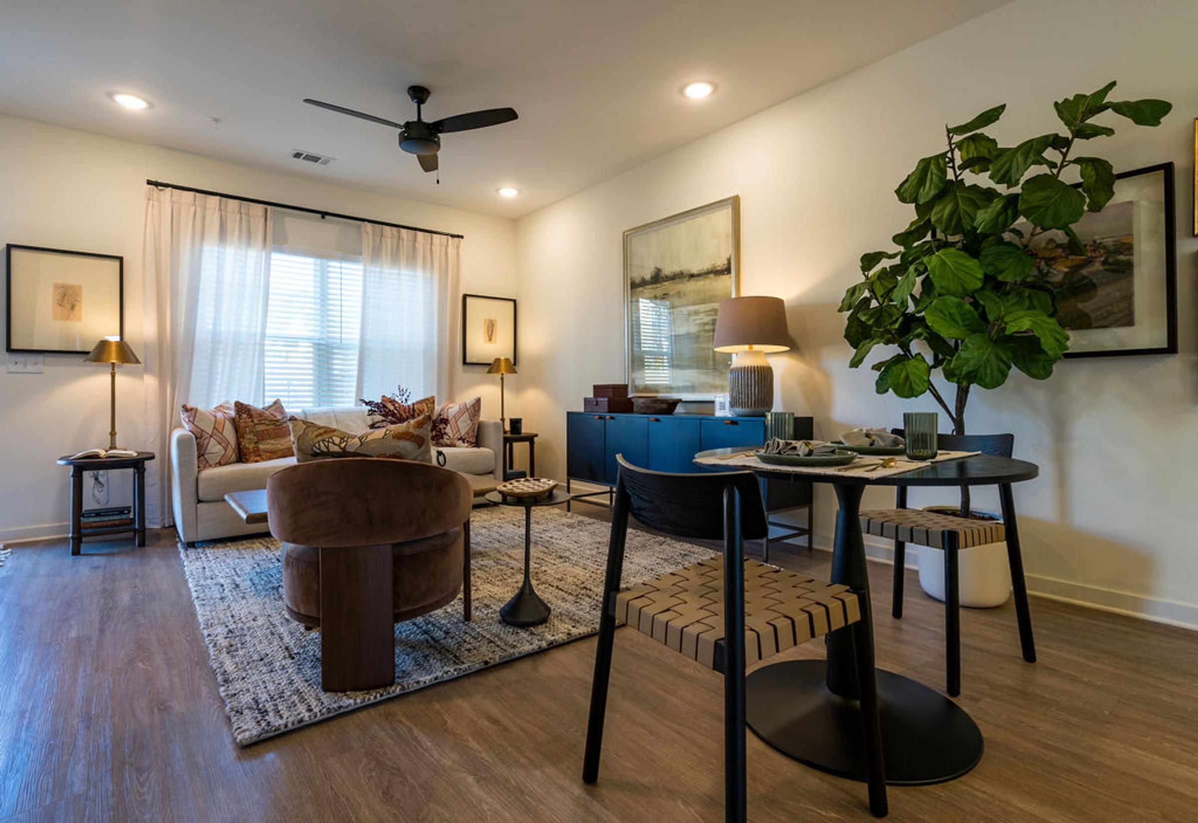 A living room with a brown chair, a white couch, a blue ottoman, and a plant.