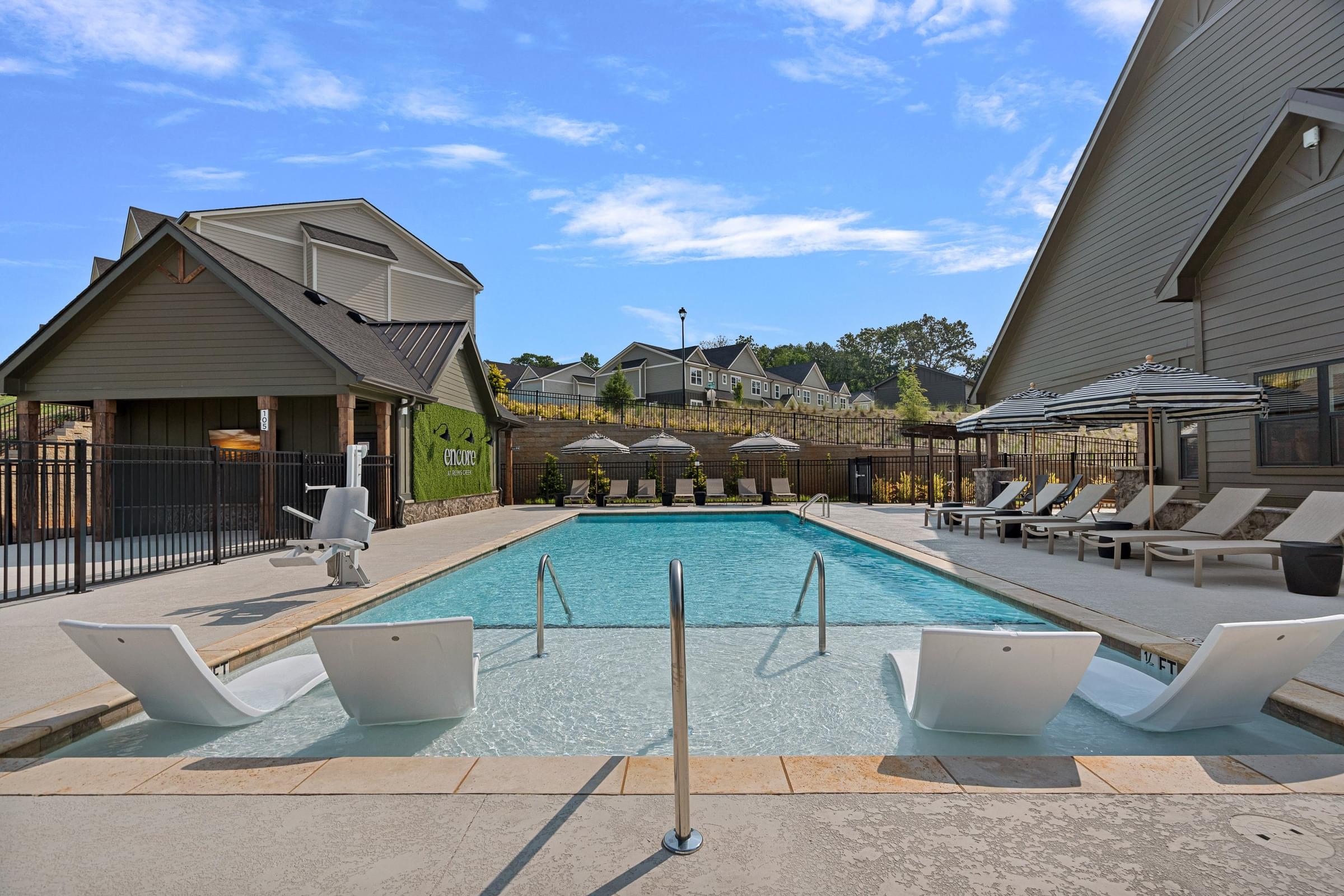 A pool with a diving board and lounge chairs.