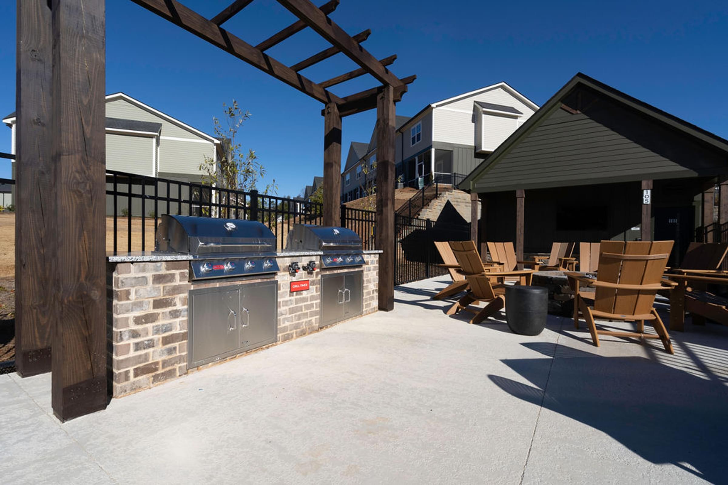 A patio with a grill and chairs under a wooden pergola.
