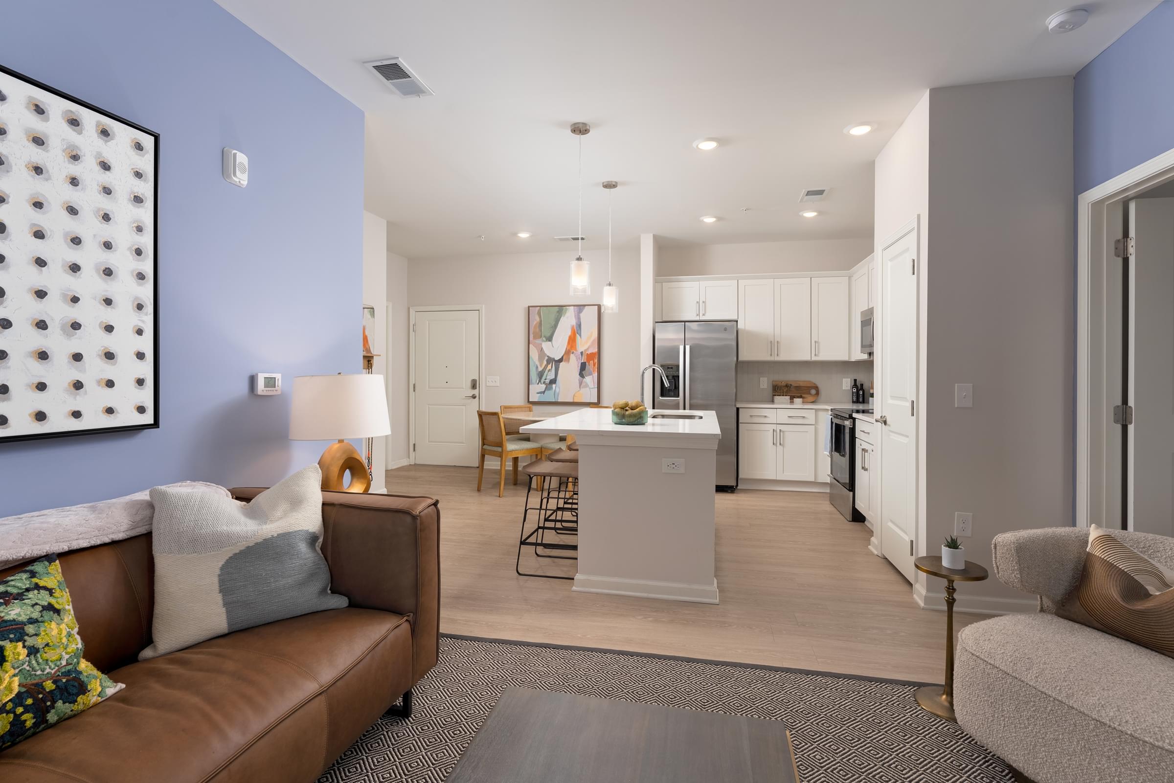 A modern living room with a brown leather couch and a kitchen in the background at Hawthorne at Holly Ridge in NC