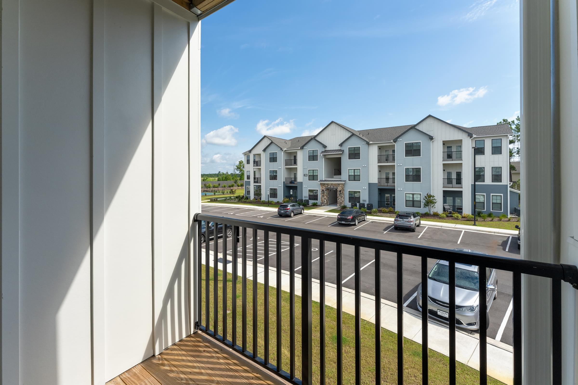 A balcony overlooks a parking lot and apartment buildings at Hawthorne at Holly Ridge in NC