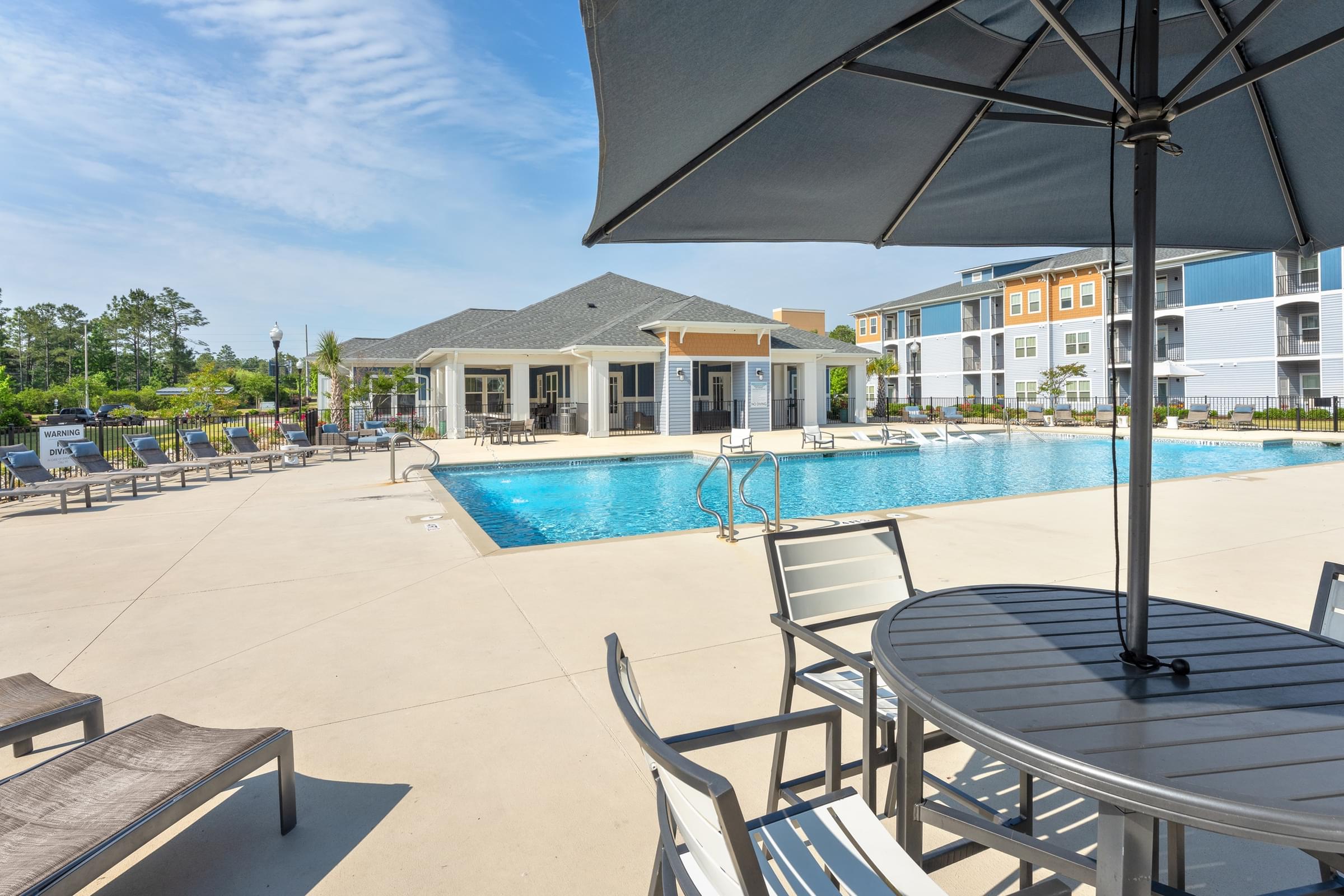 A pool area with a table and chairs and a building in the background.