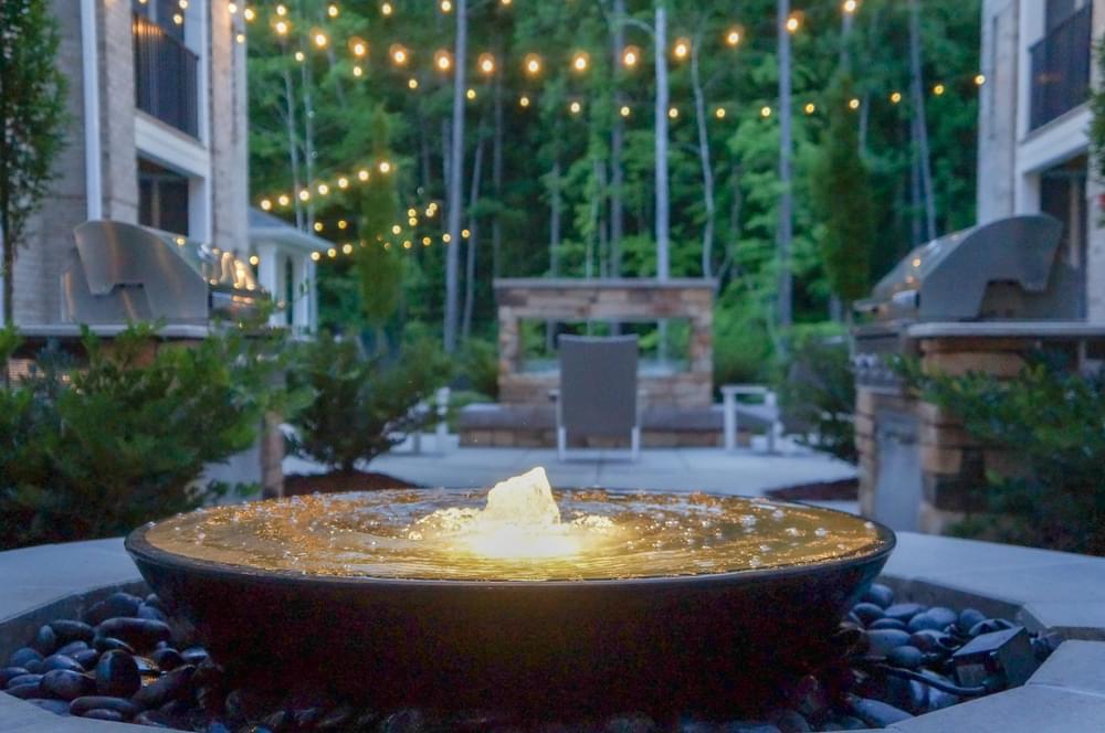 a fire pit with water on a patio with lights in the background
