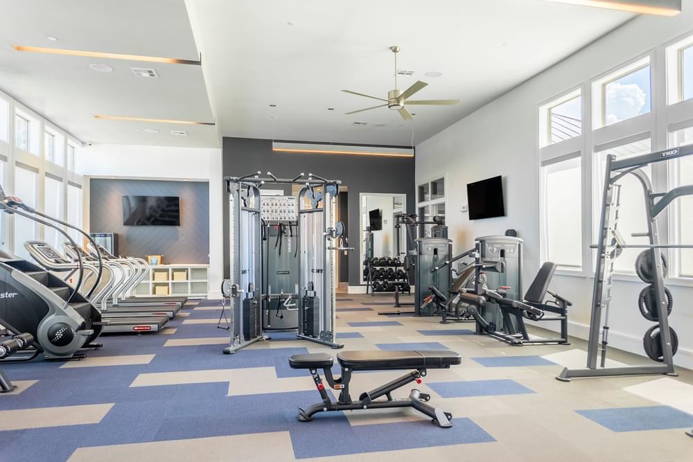 a gym with weights and cardio equipment in a large room with windows