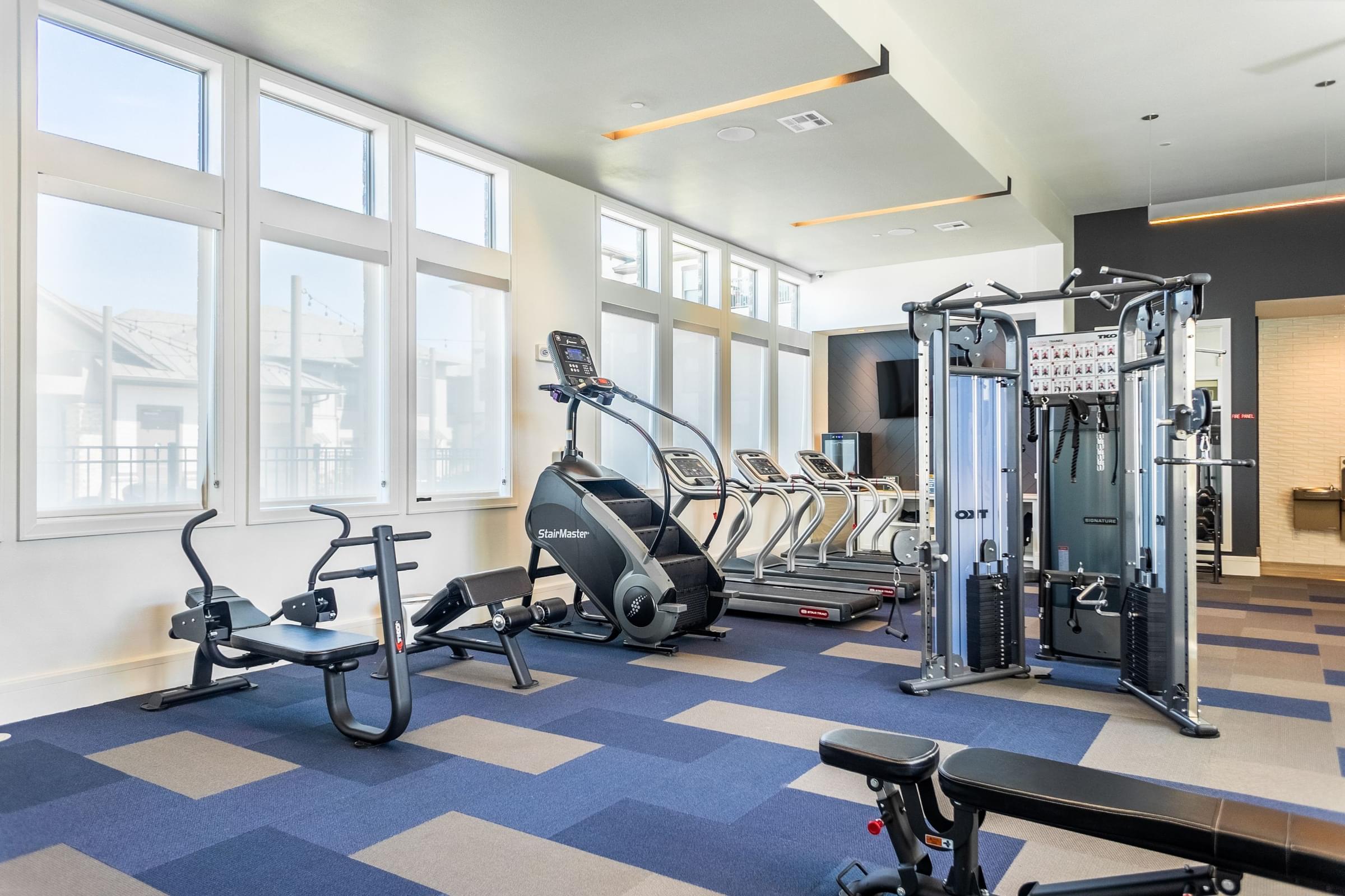 a gym with cardio machines and weights in a room with windows