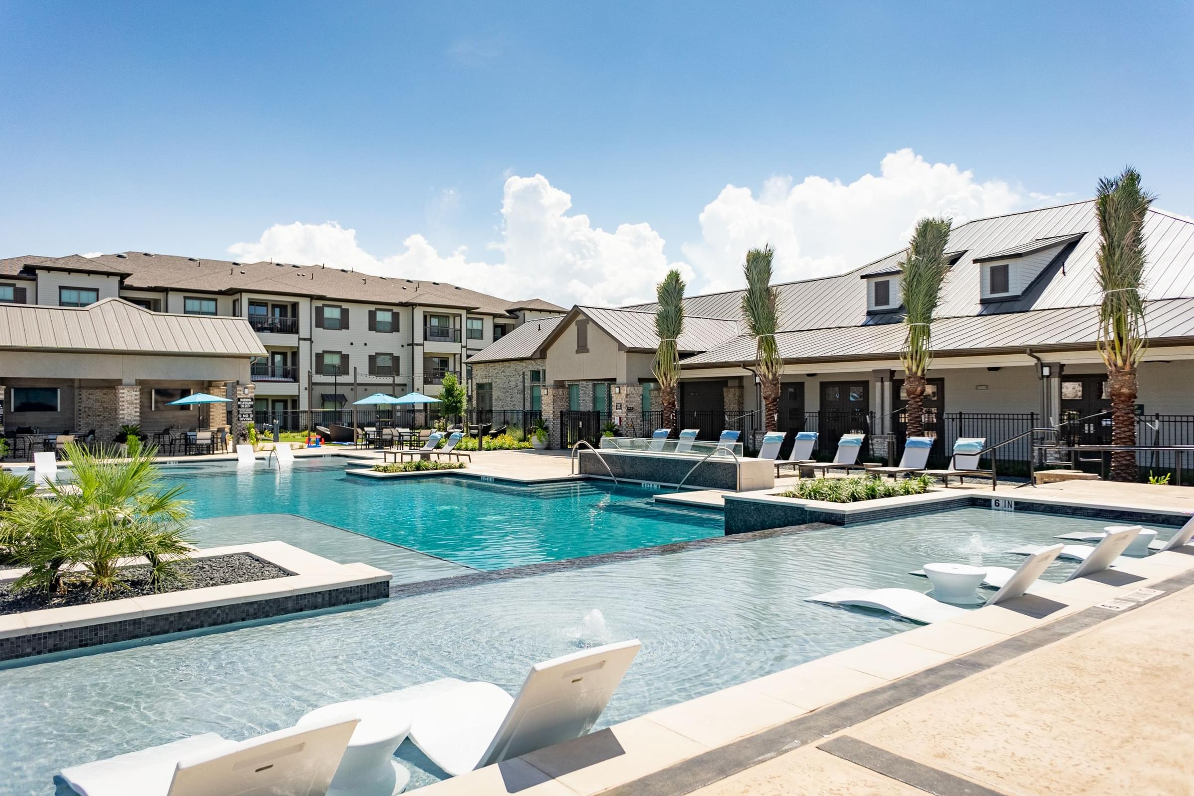 a large swimming pool with lounge chairs and buildings in the background