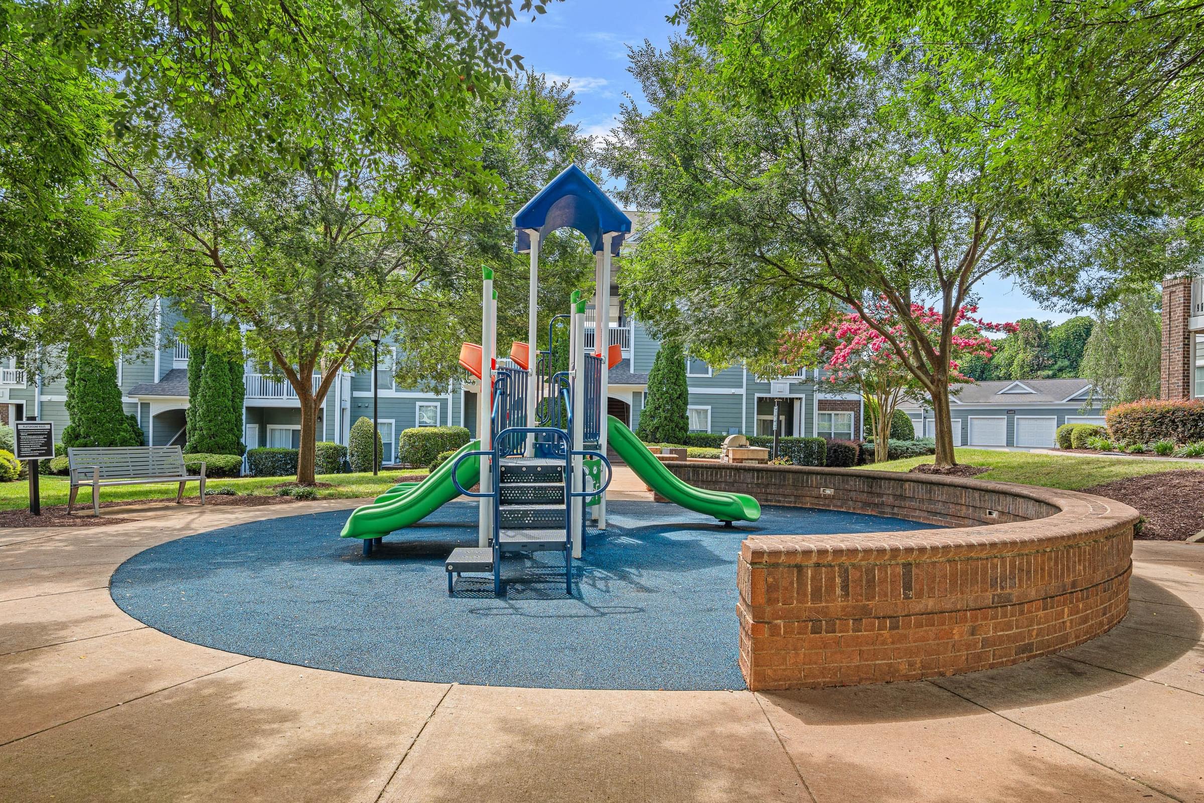 A playground with a blue and green slide and a brick wall.