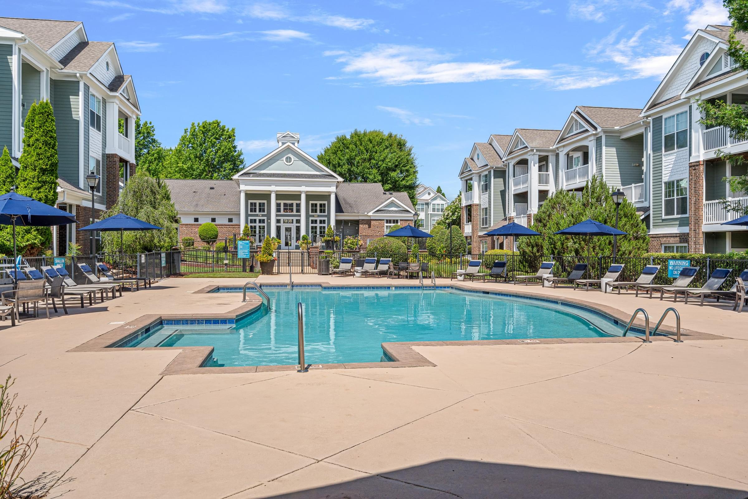 A large swimming pool surrounded by a patio with chairs and umbrellas.