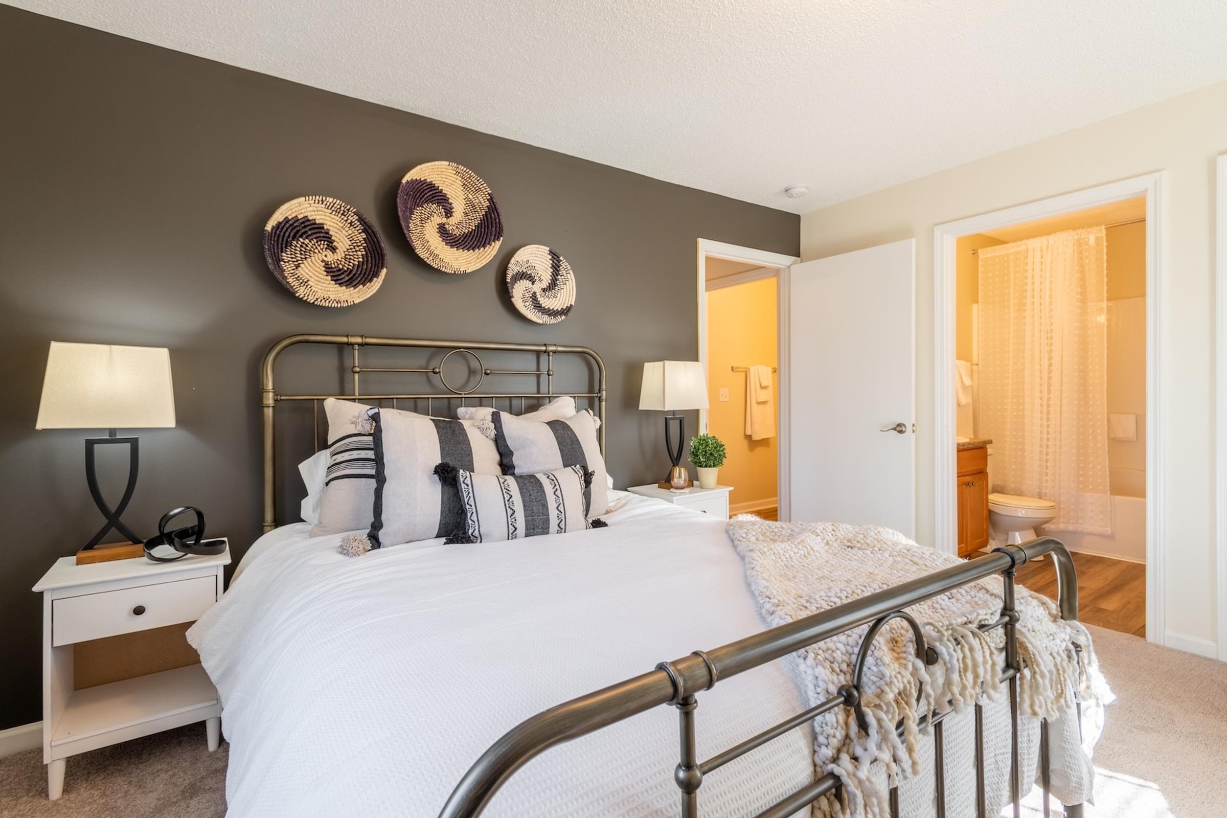 A bedroom with a white bed and a white nightstand with a lamp on it