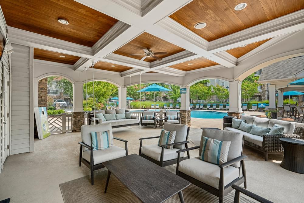 a covered patio with couches and chairs and a pool in the background