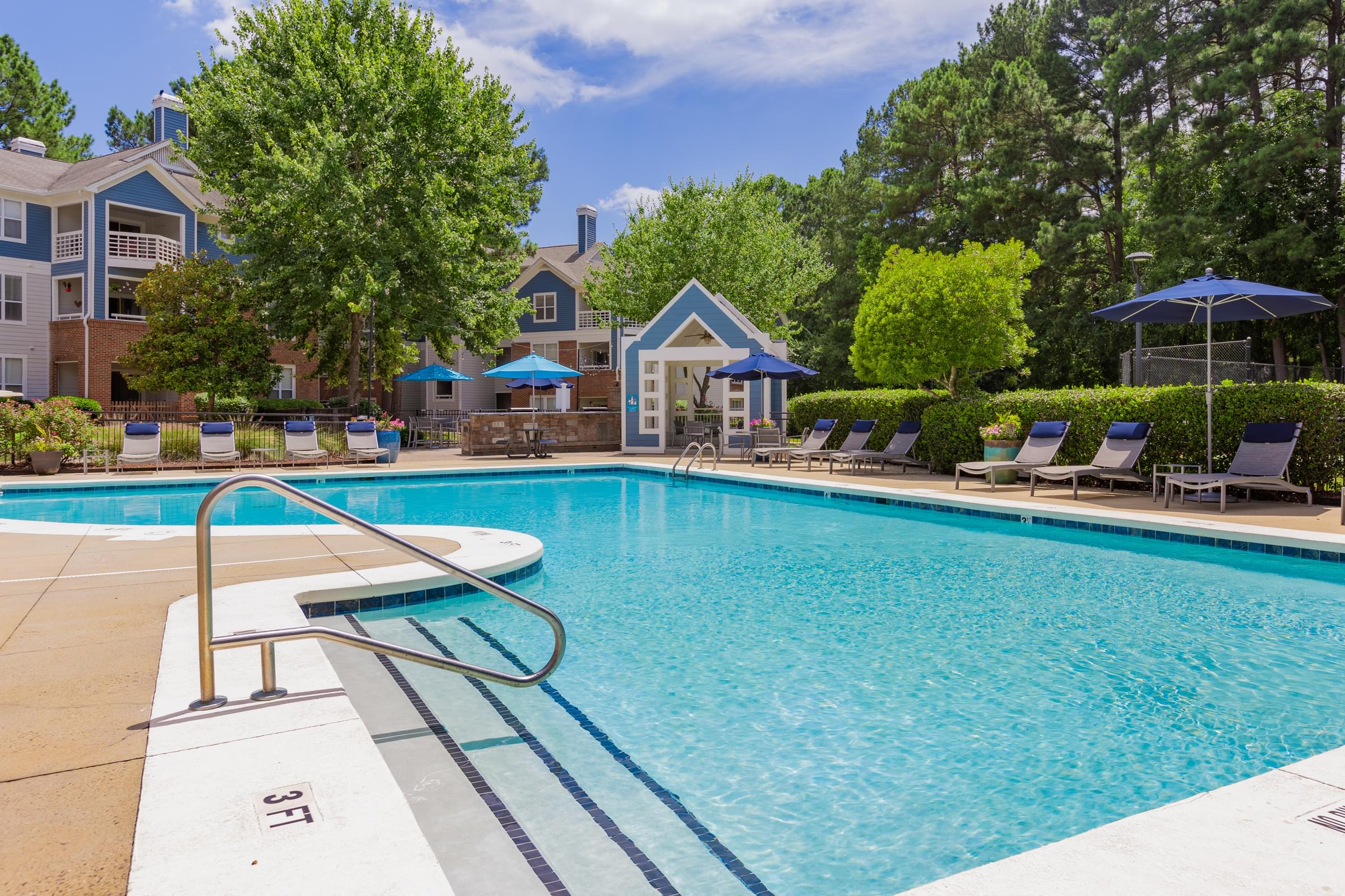 a swimming pool with chairs and umbrellas in front of apartment buildings