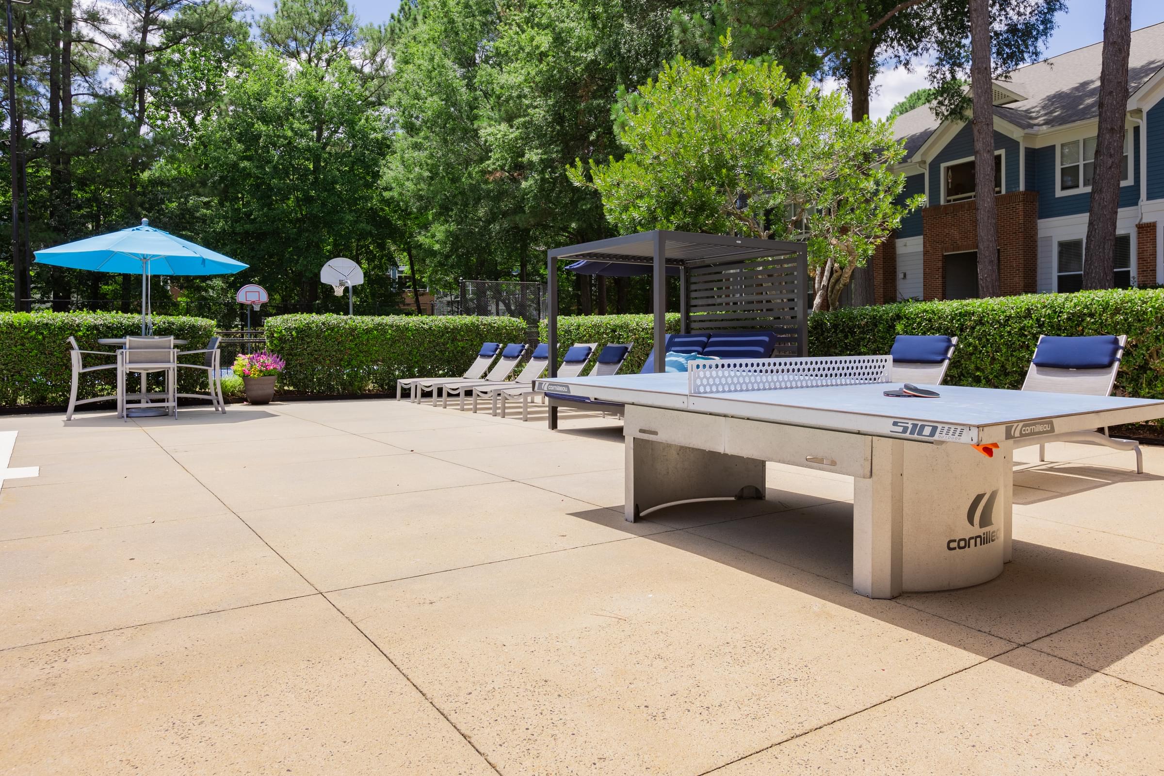 a ping pong table in a courtyard with chairs and umbrellas