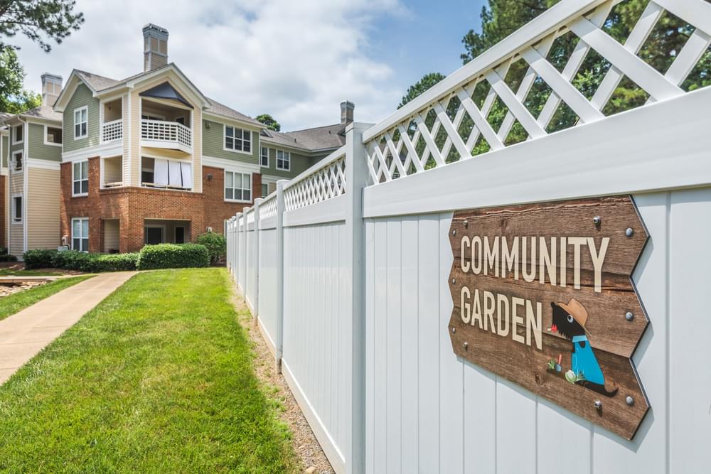 a community garden sign on a white fence in front of an apartment building