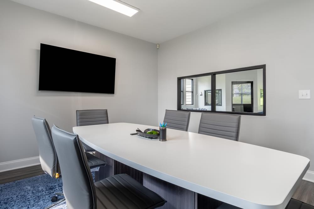 a meeting room with a large white table and chairs and a flat screen tv on the wall
