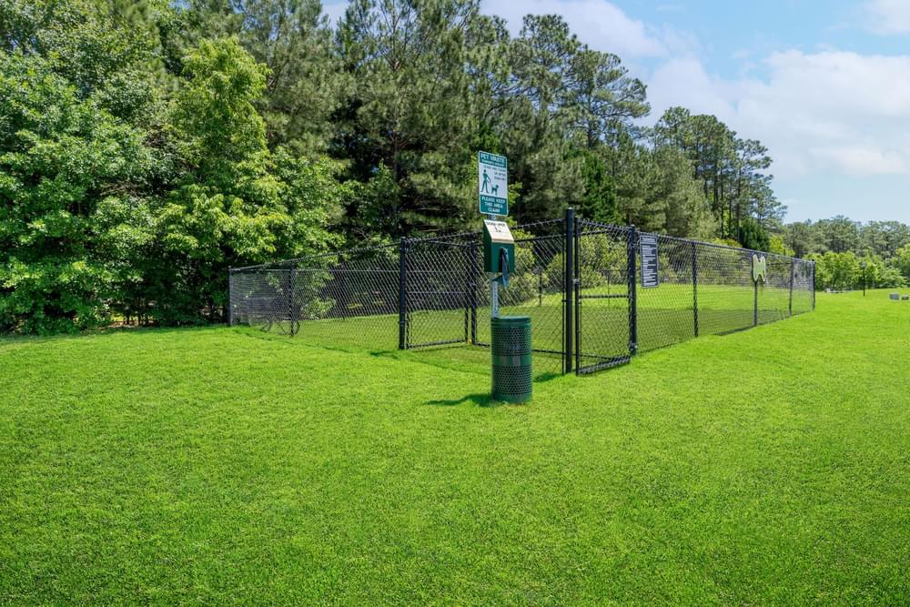 a park with a fence and a trash can in the grass