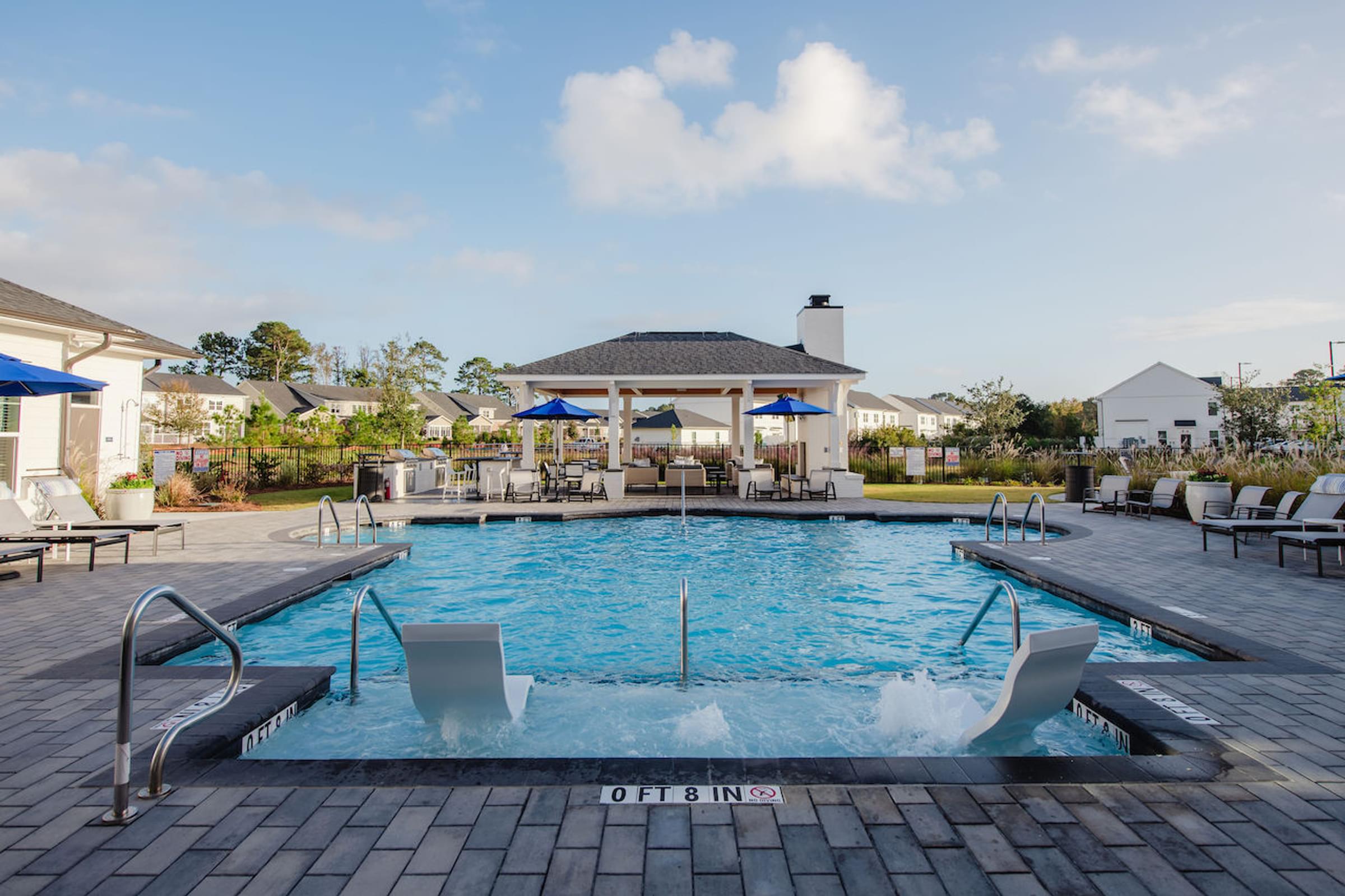 a swimming pool with lounge chairs and umbrellas in front of a resort style clubhouse