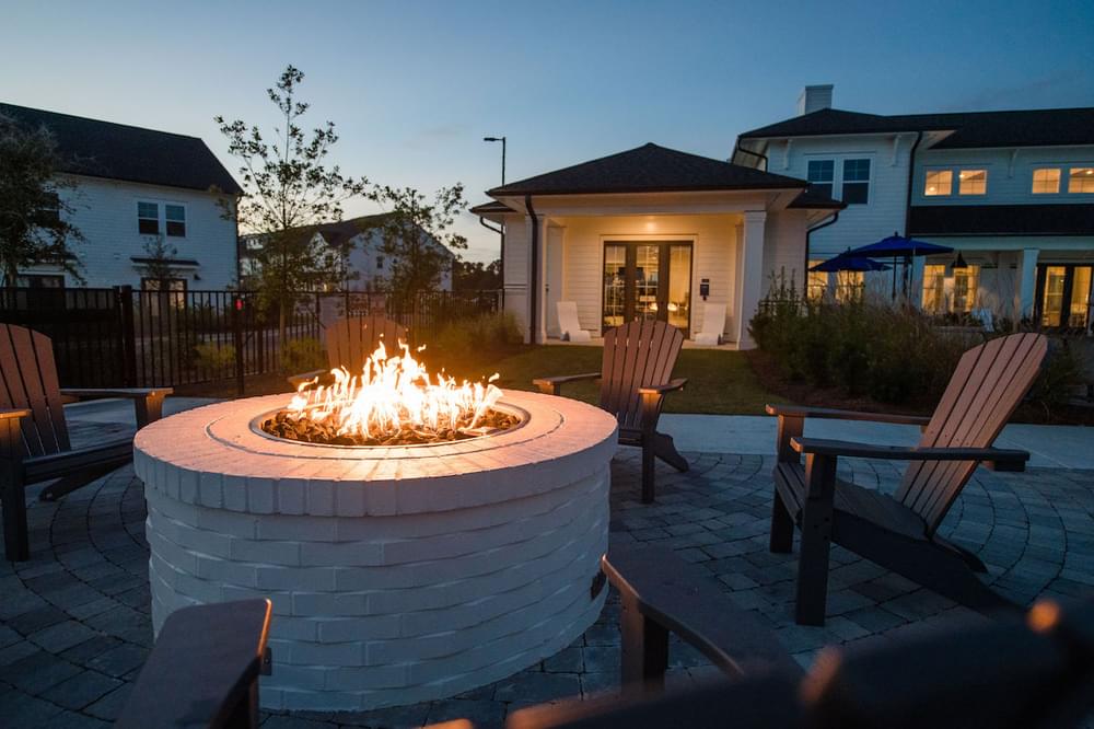 a fire pit in a backyard with chairs and a house in the background