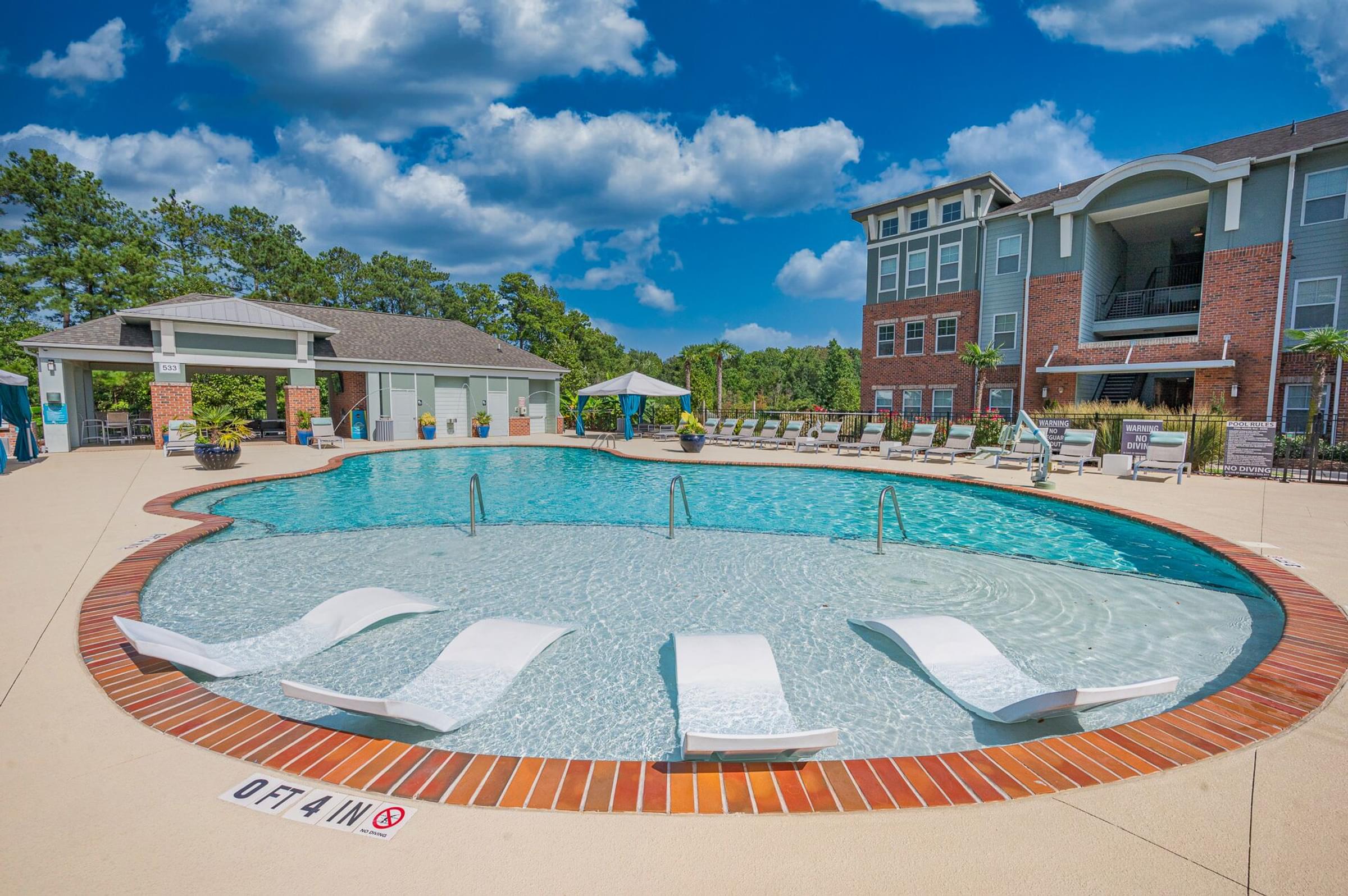 A large outdoor swimming pool with lounge chairs and a building in the background.