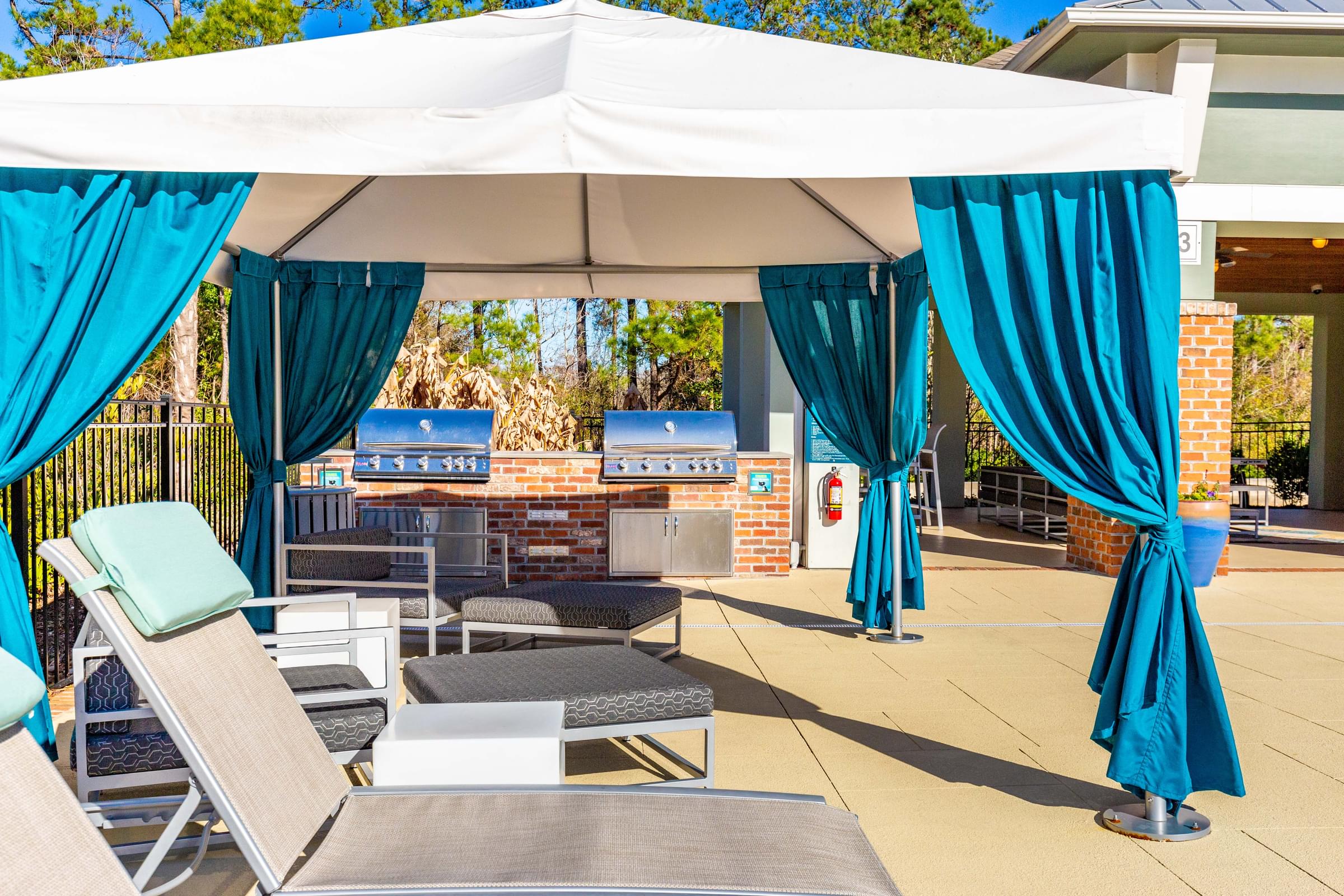 A white canopy with blue curtains is set up over a table and chairs