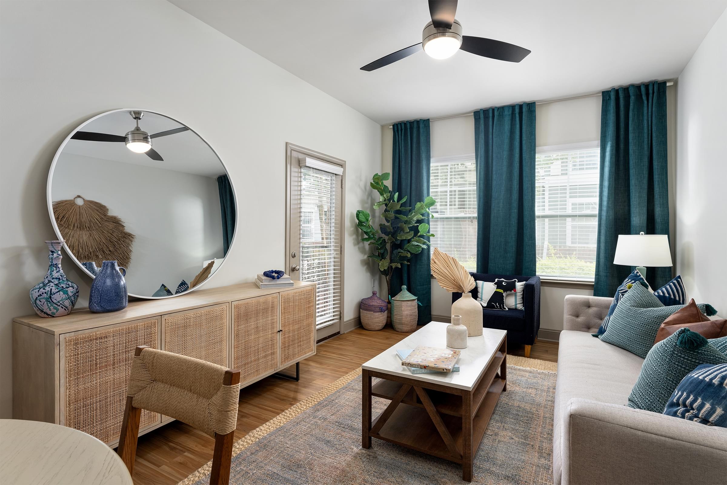 A living room with a round mirror, a wooden cabinet, a coffee table, a couch, and a potted plant.