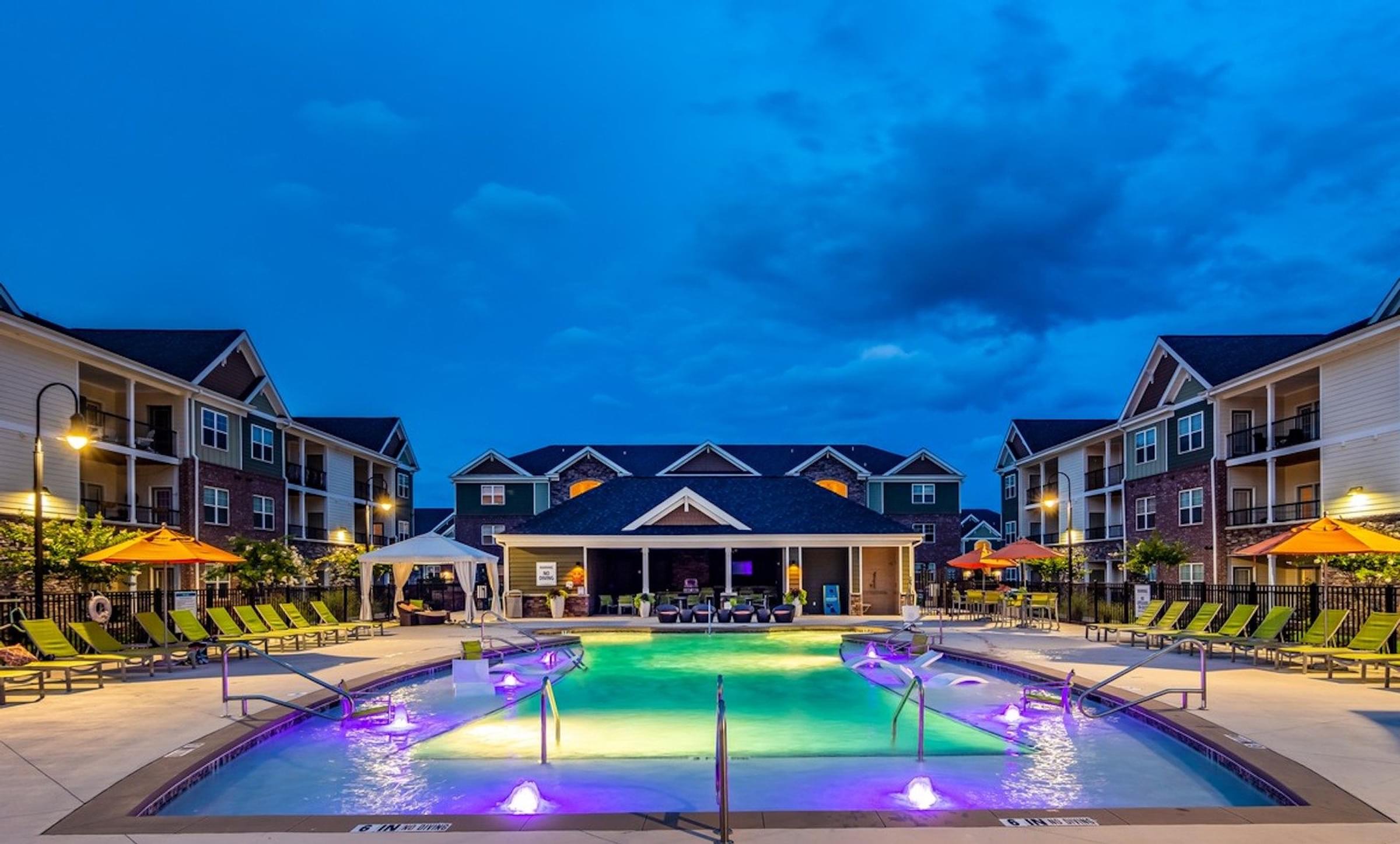 a swimming pool at night in front of an apartment building