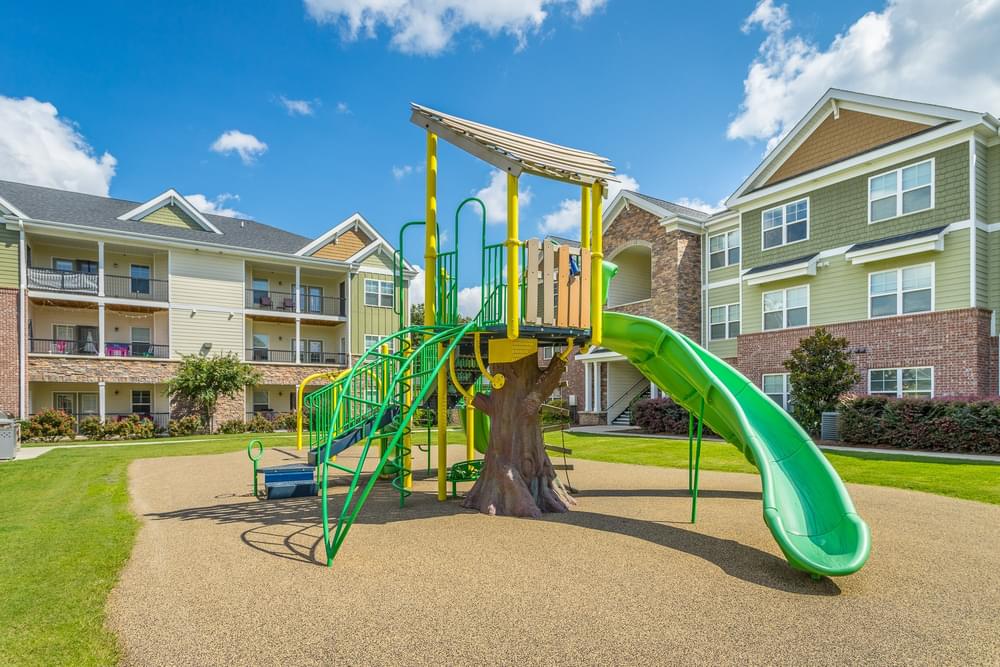 a playground with a green slide in front of an apartment building