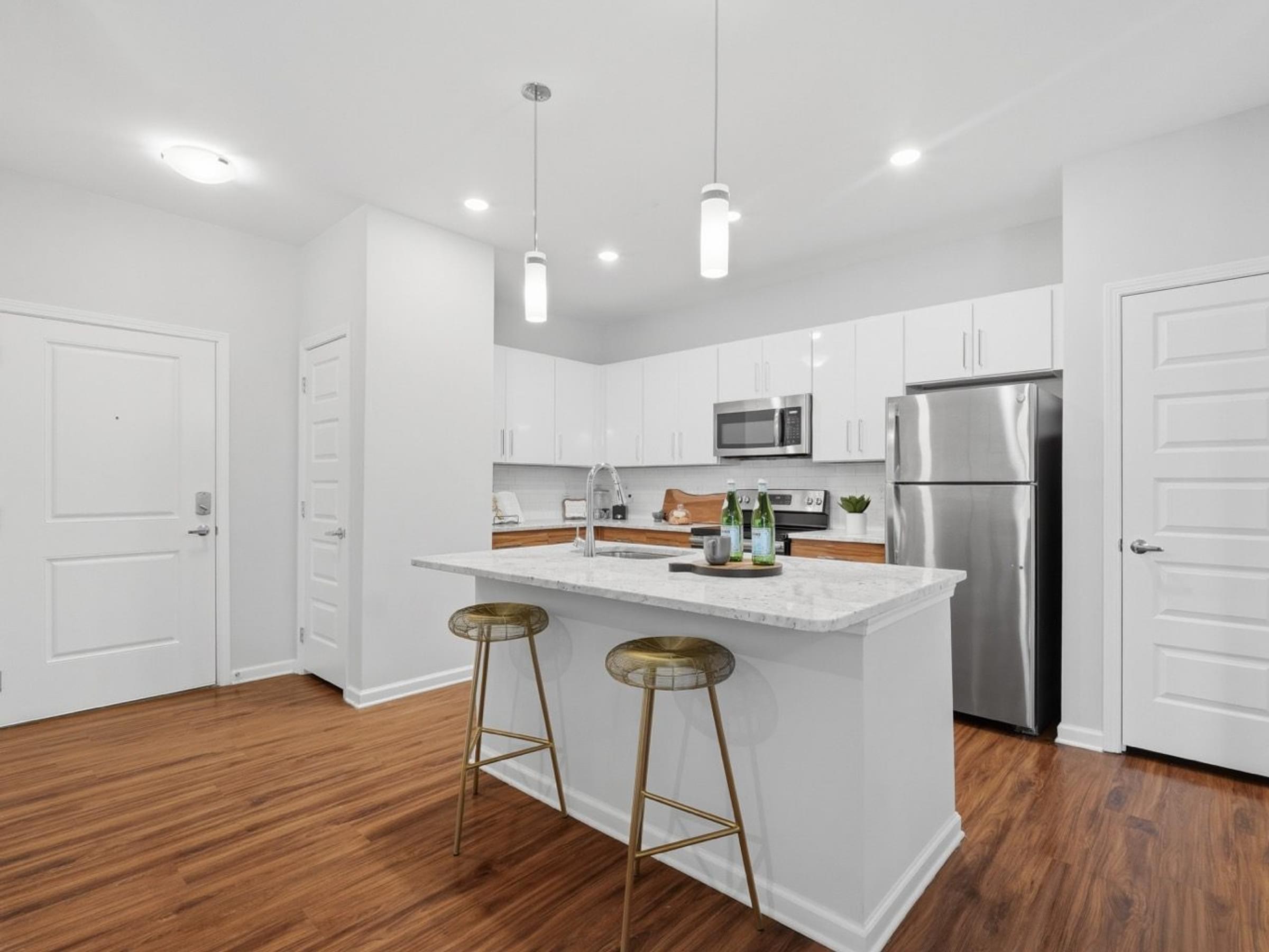 A kitchen with white cabinets and a white island with two stools.