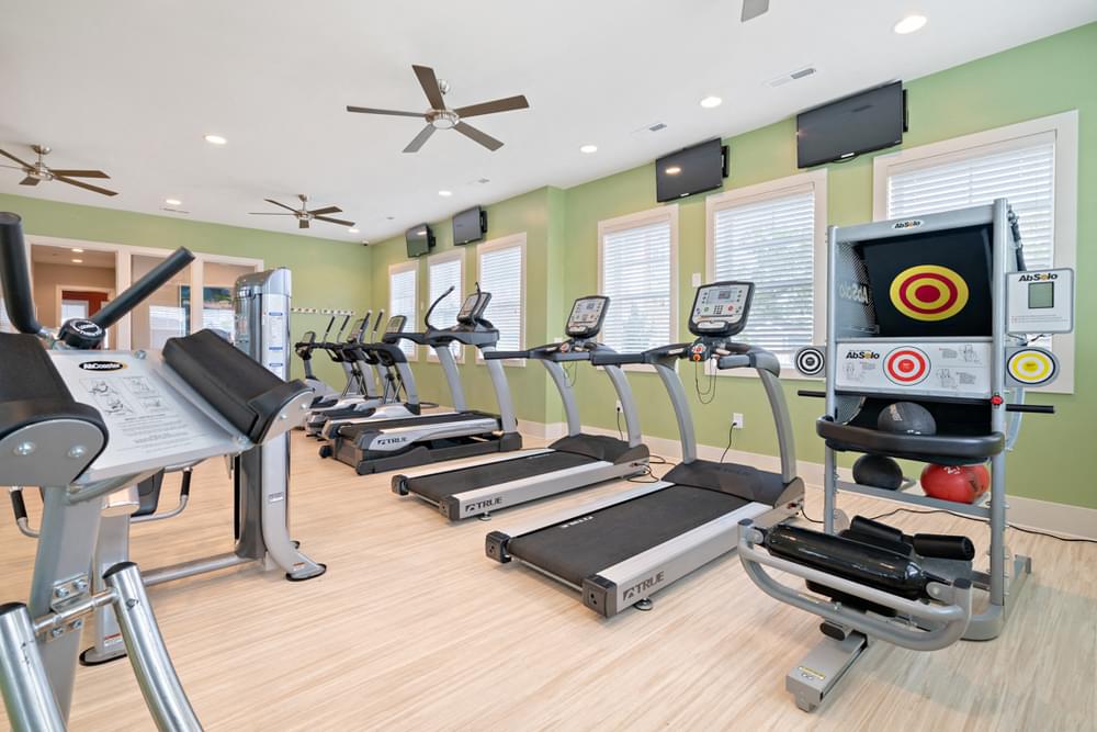 a gym with various cardio equipment on the floor and windows