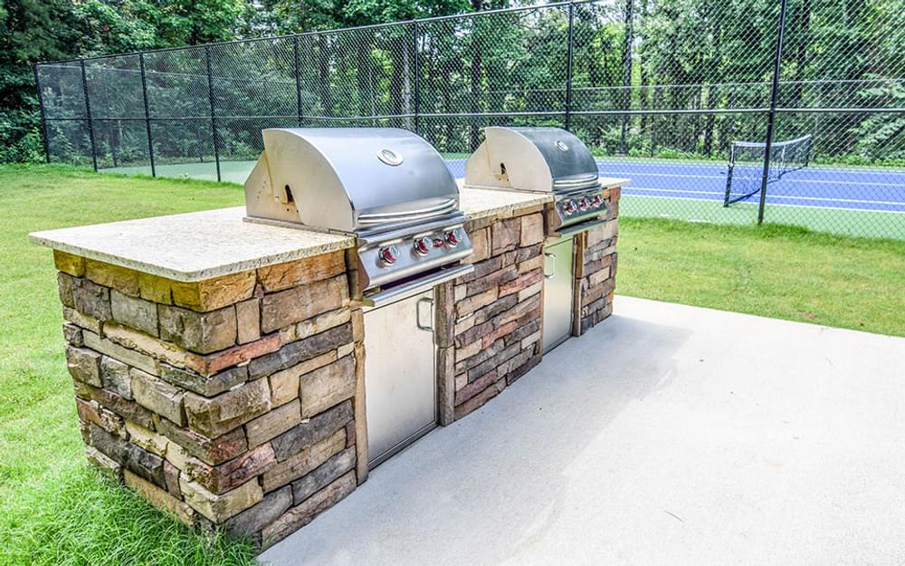 two bbq pits in a backyard with a tennis court