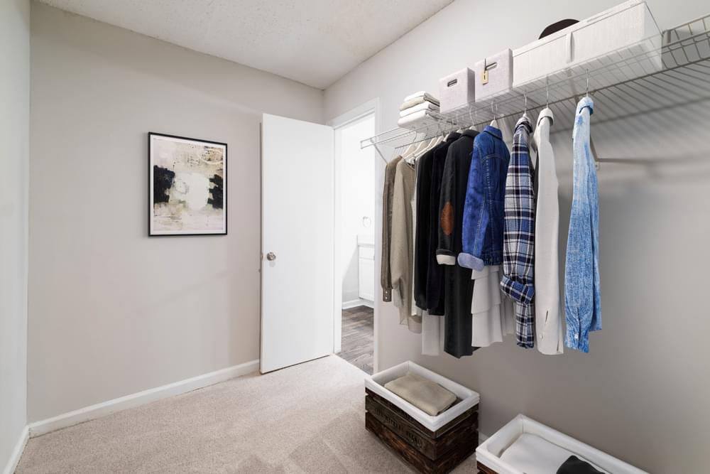a walk in closet with clothes hanging on a rack and a bathroom with a sink