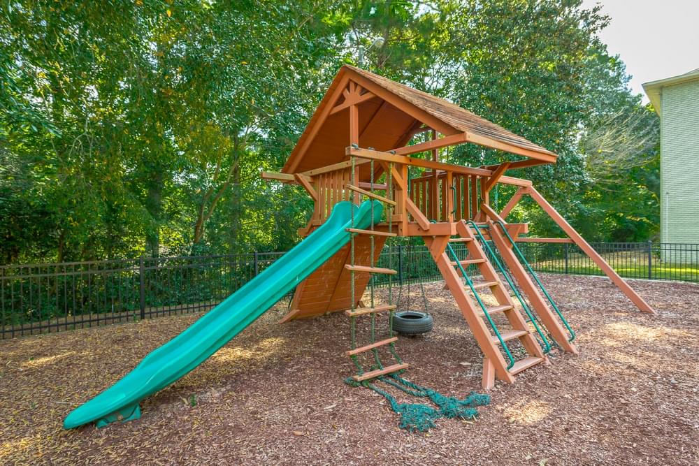 a playground with a wooden playset with a green slide