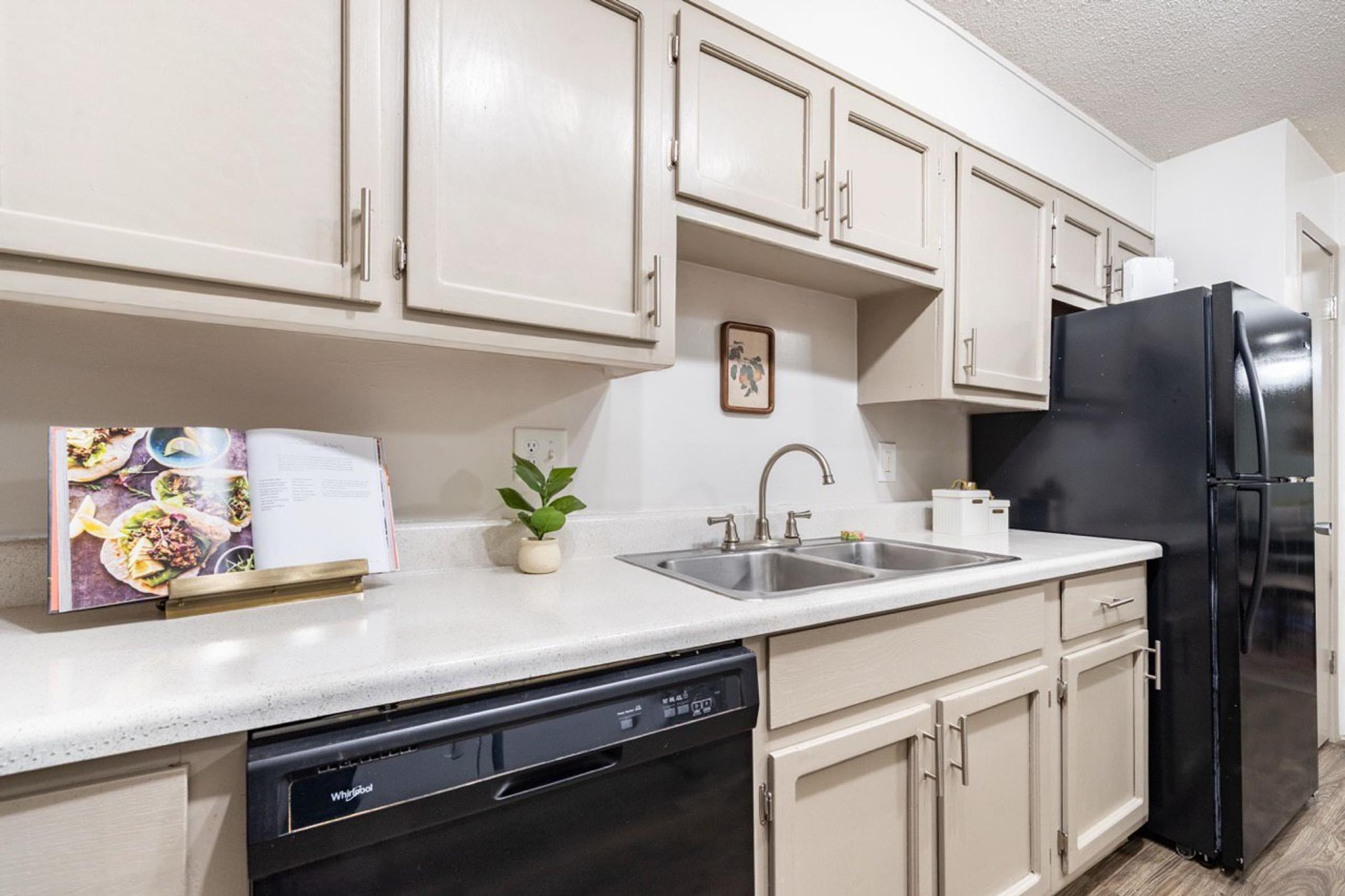 A kitchen with a black refrigerator, white countertops, and beige cabinets.