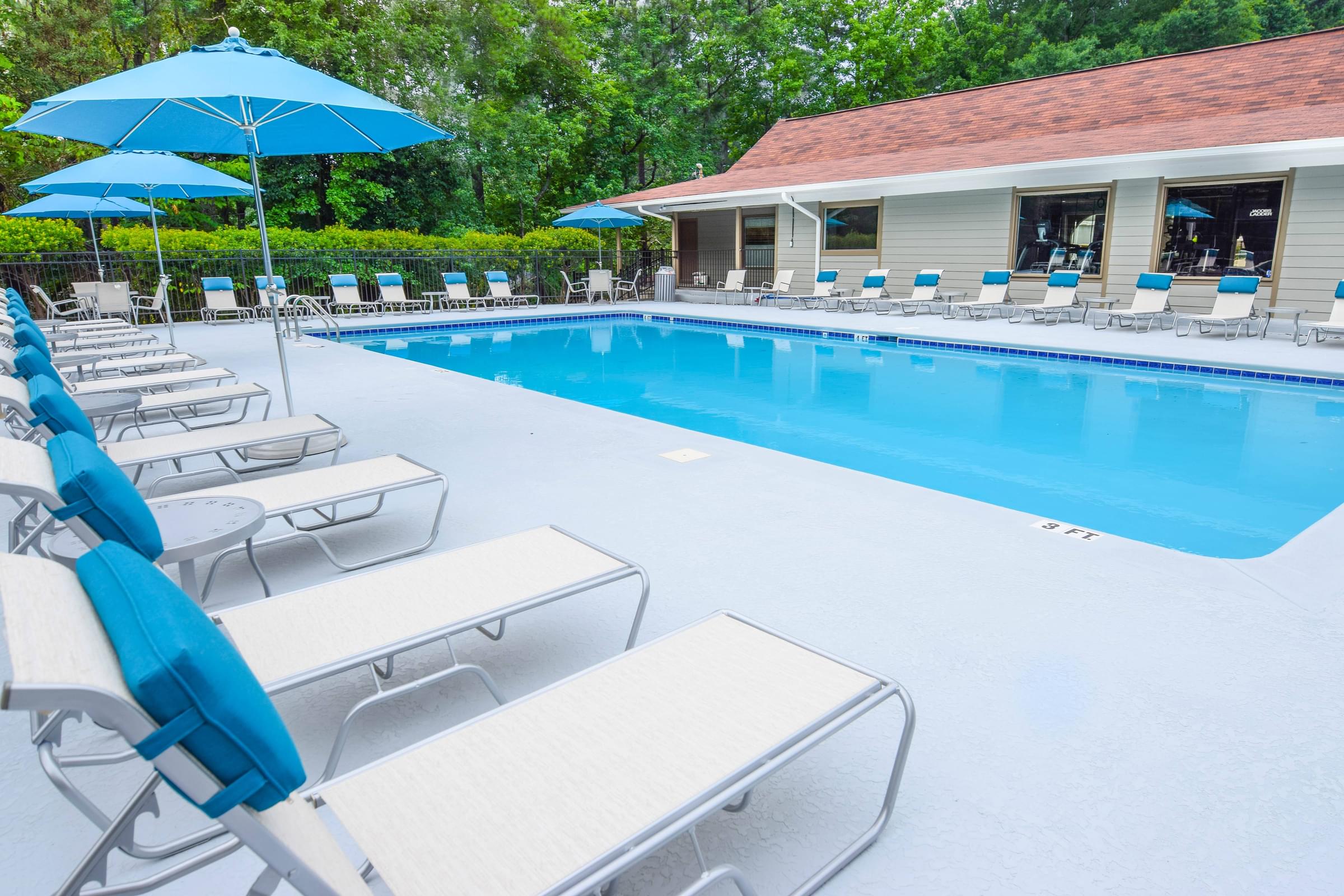 A pool with sun loungers and umbrellas in front of a building.