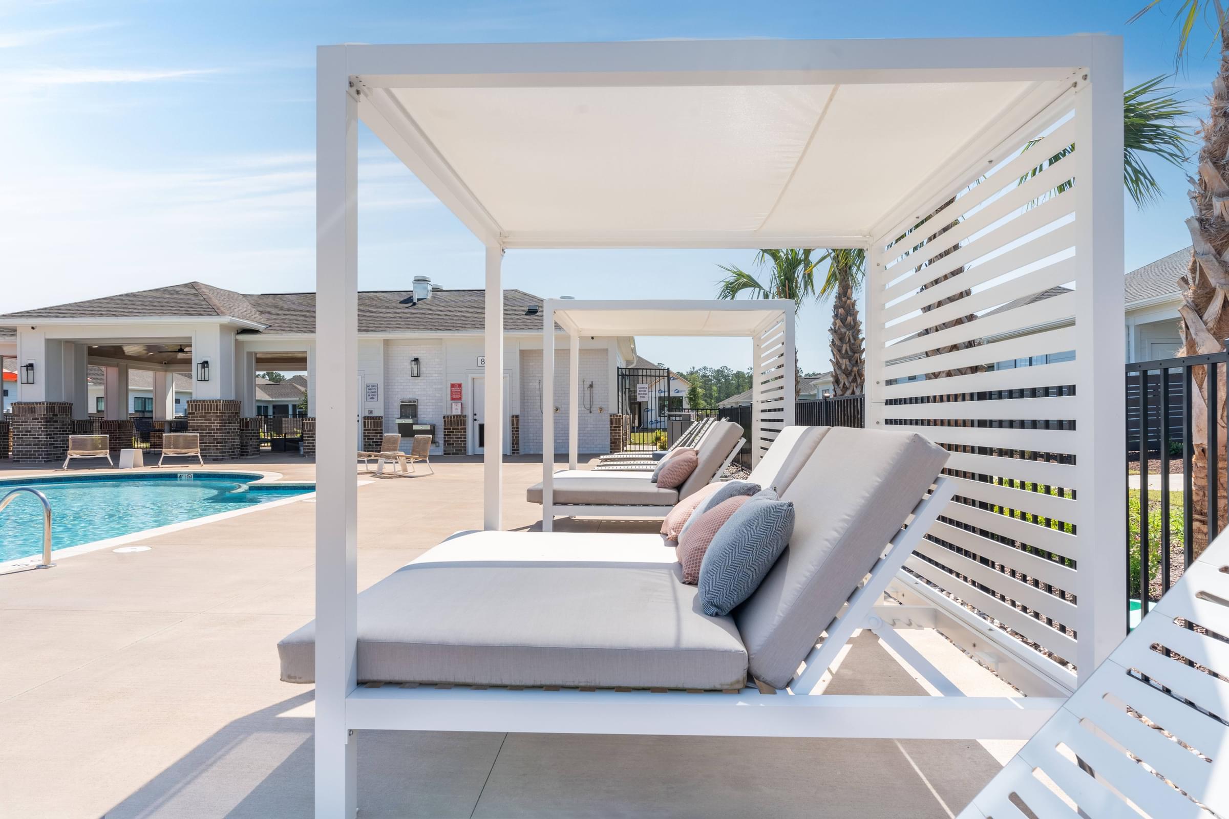 A white lounge chair with a grey cushion is in the foreground of a poolside area.