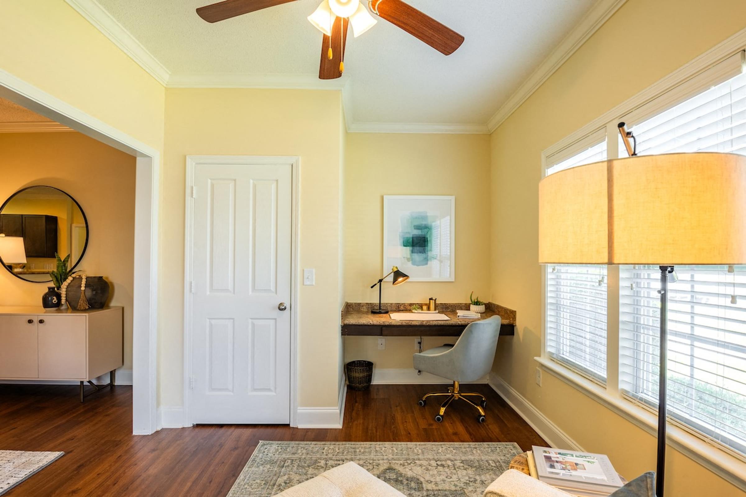 a living room with a desk and a ceiling fan