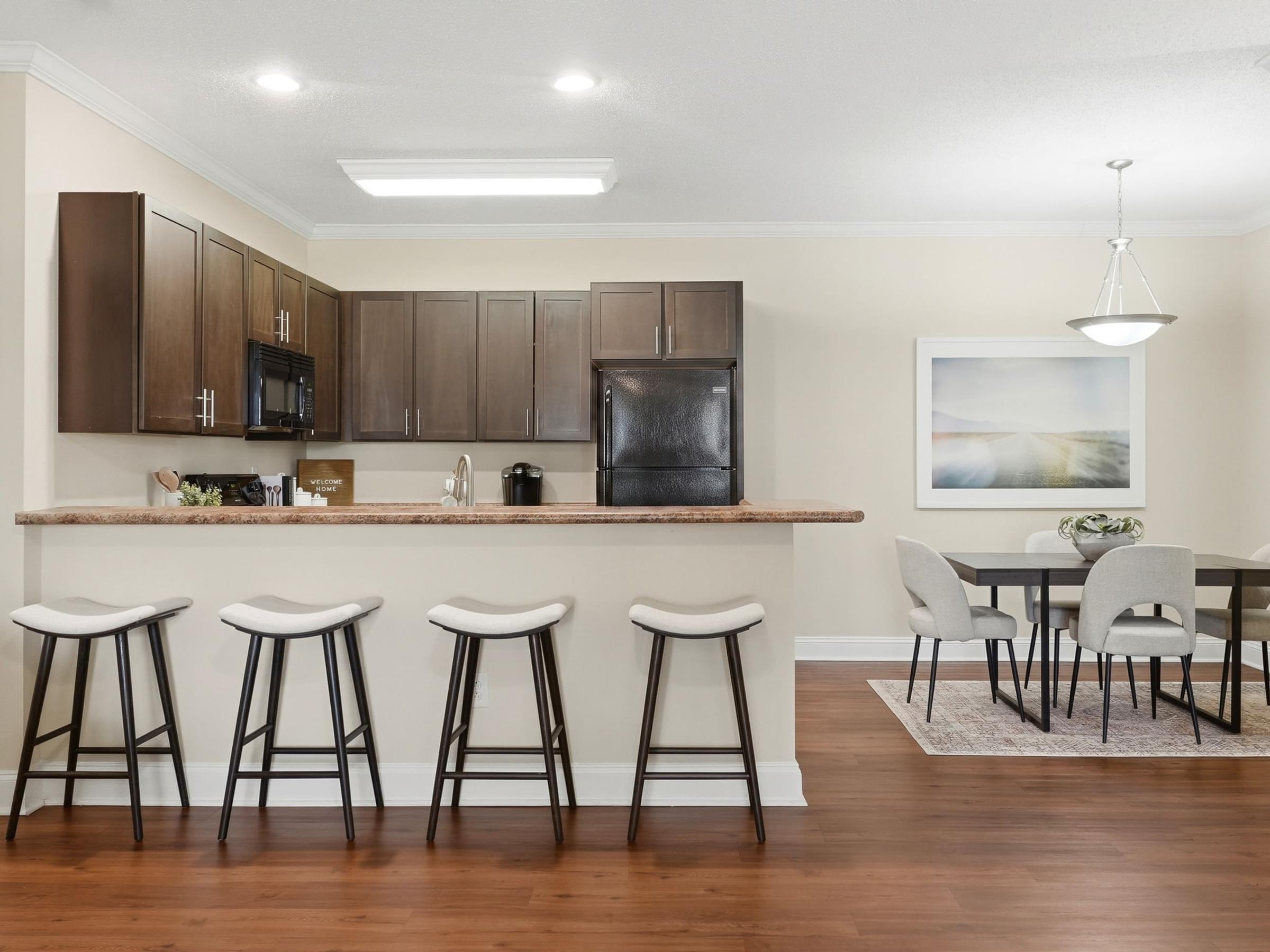 A kitchen with brown cabinets and a bar area with three stools.