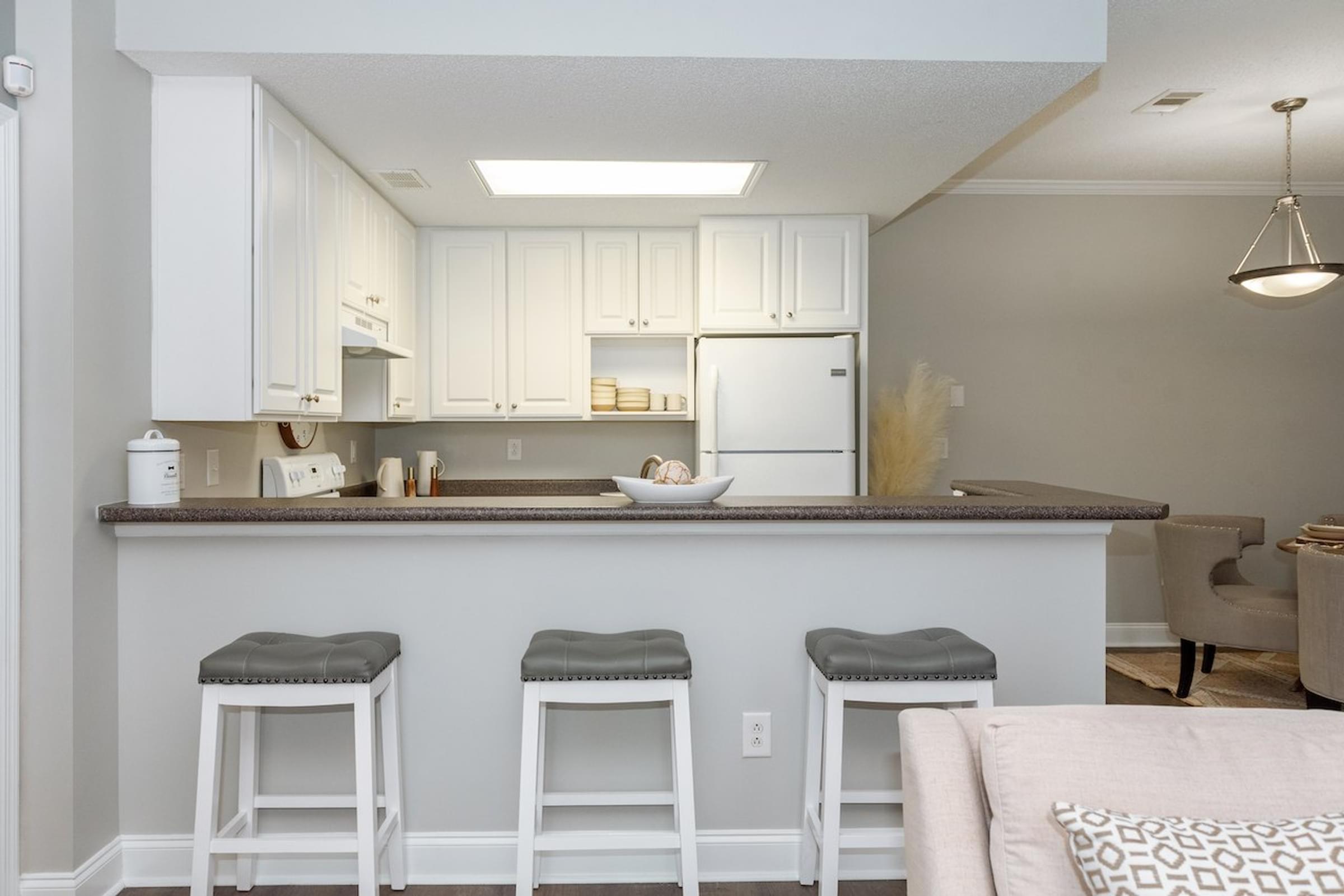a kitchen with white cabinets and a bar with three stools