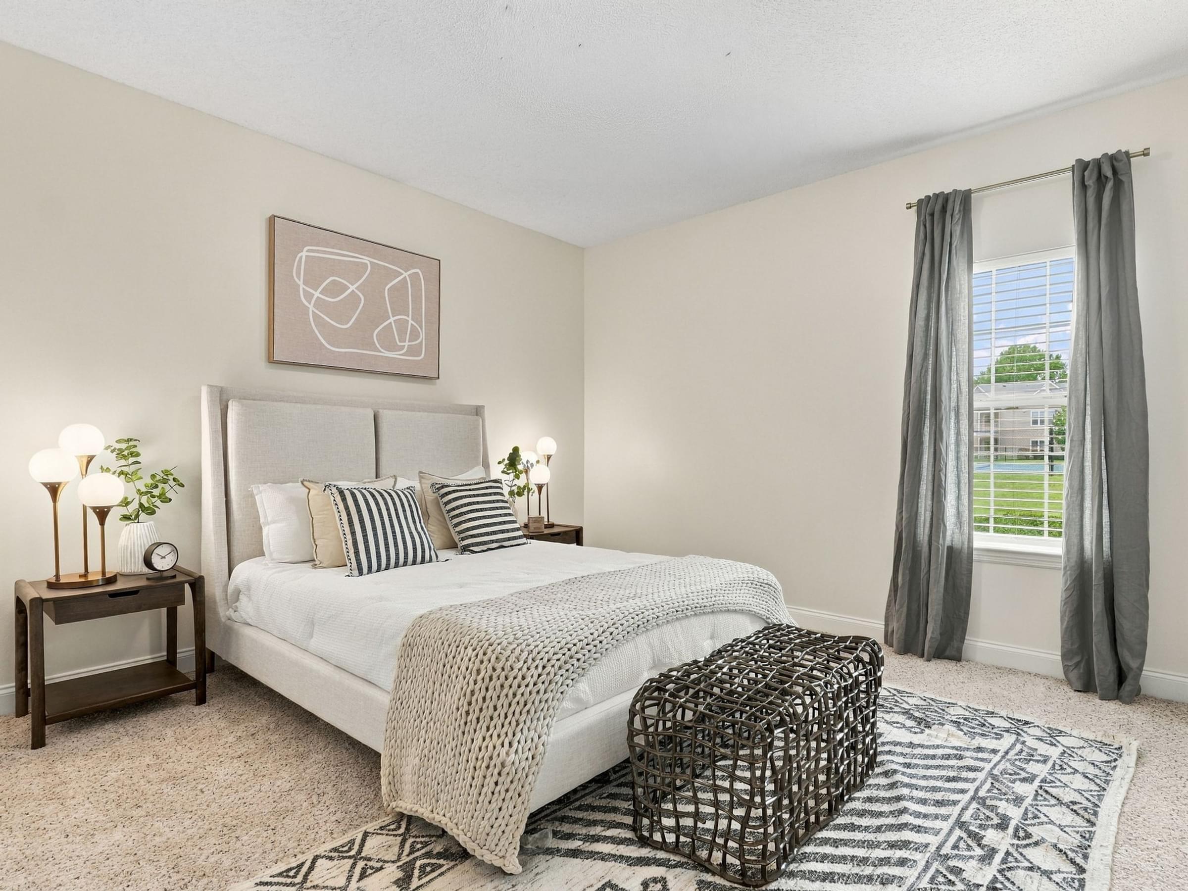 A bedroom with a large bed, a nightstand with a lamp, and a window with curtains.