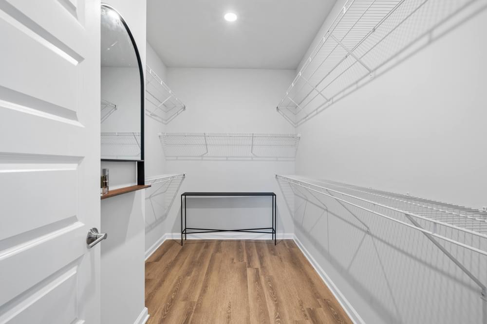 a walk in closet with white walls and a wooden floor