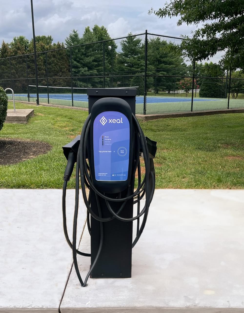 a black ev charging station with a tennis court in the background