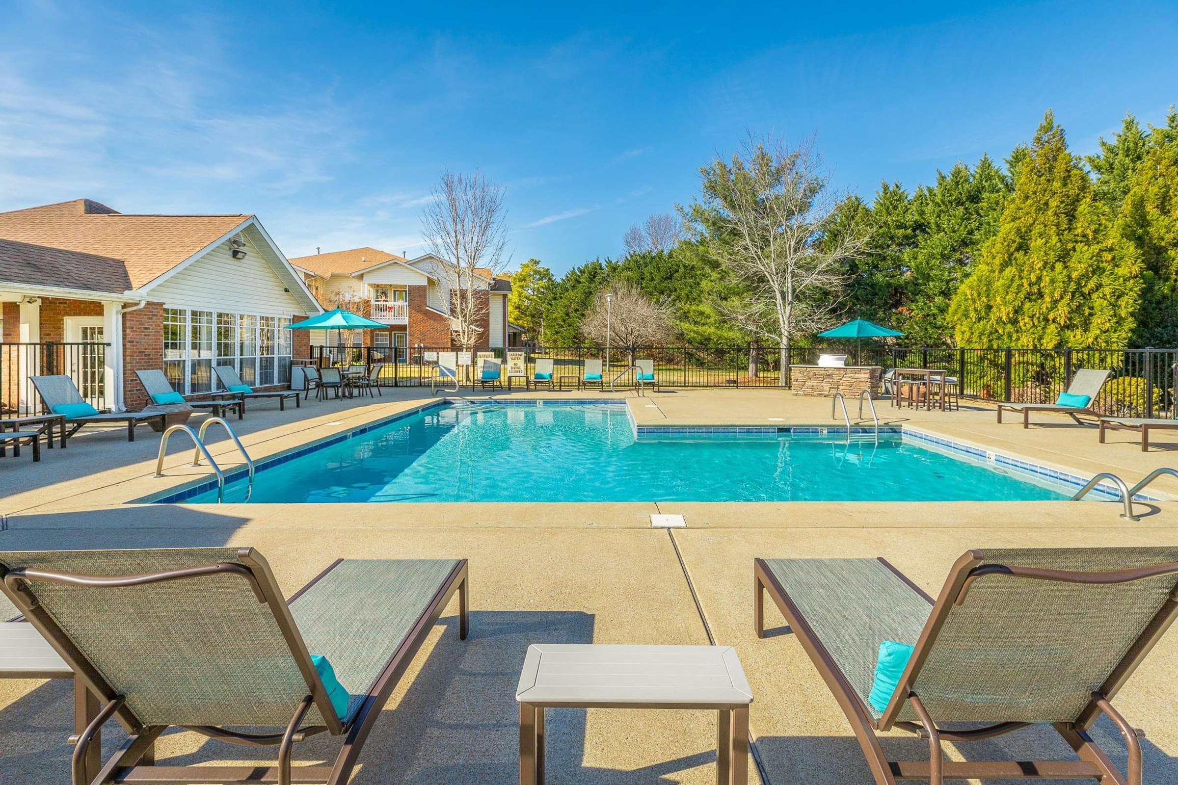 A pool surrounded by chairs and trees.