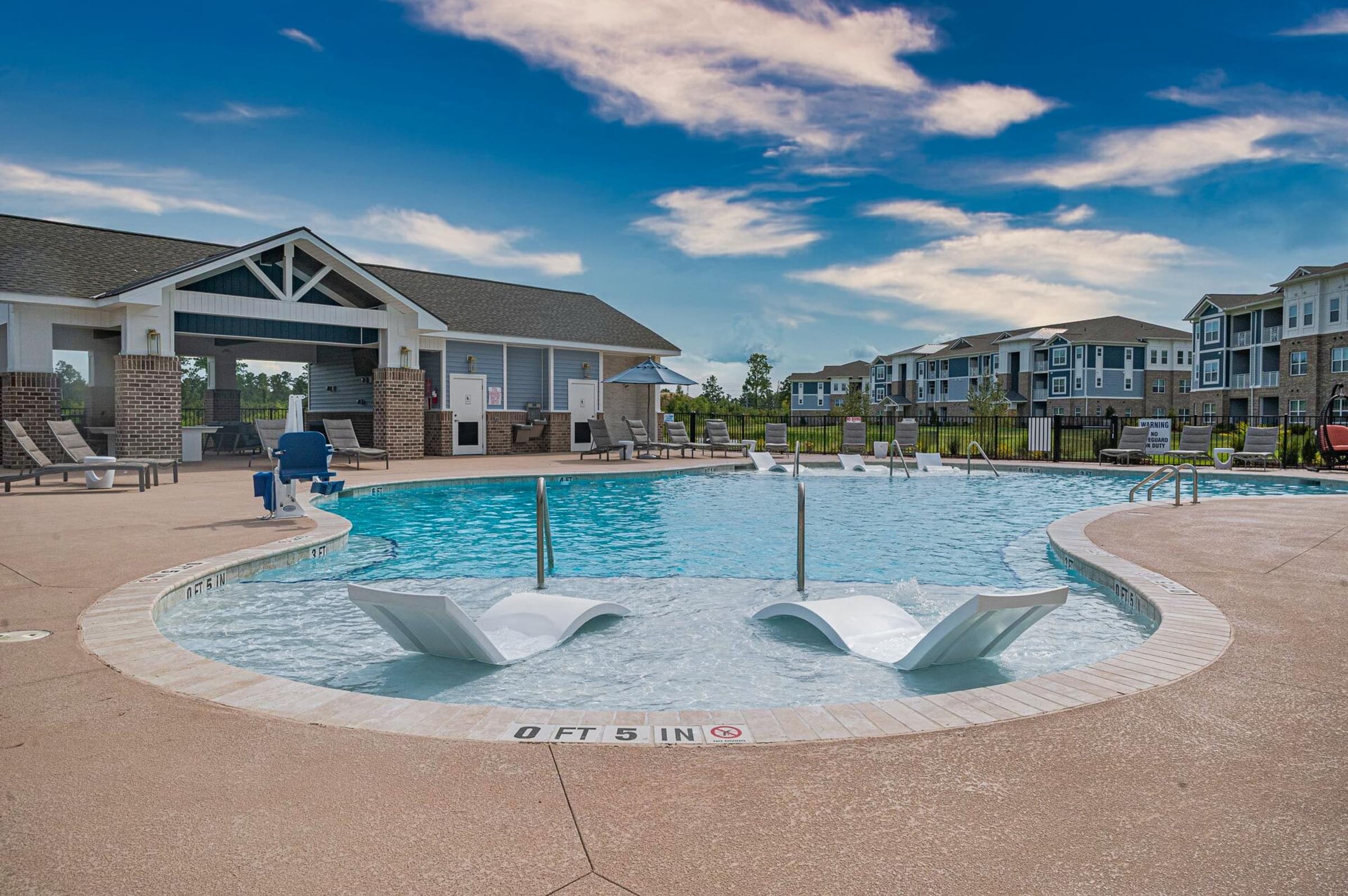 a pool with two chairs in front of an apartment building